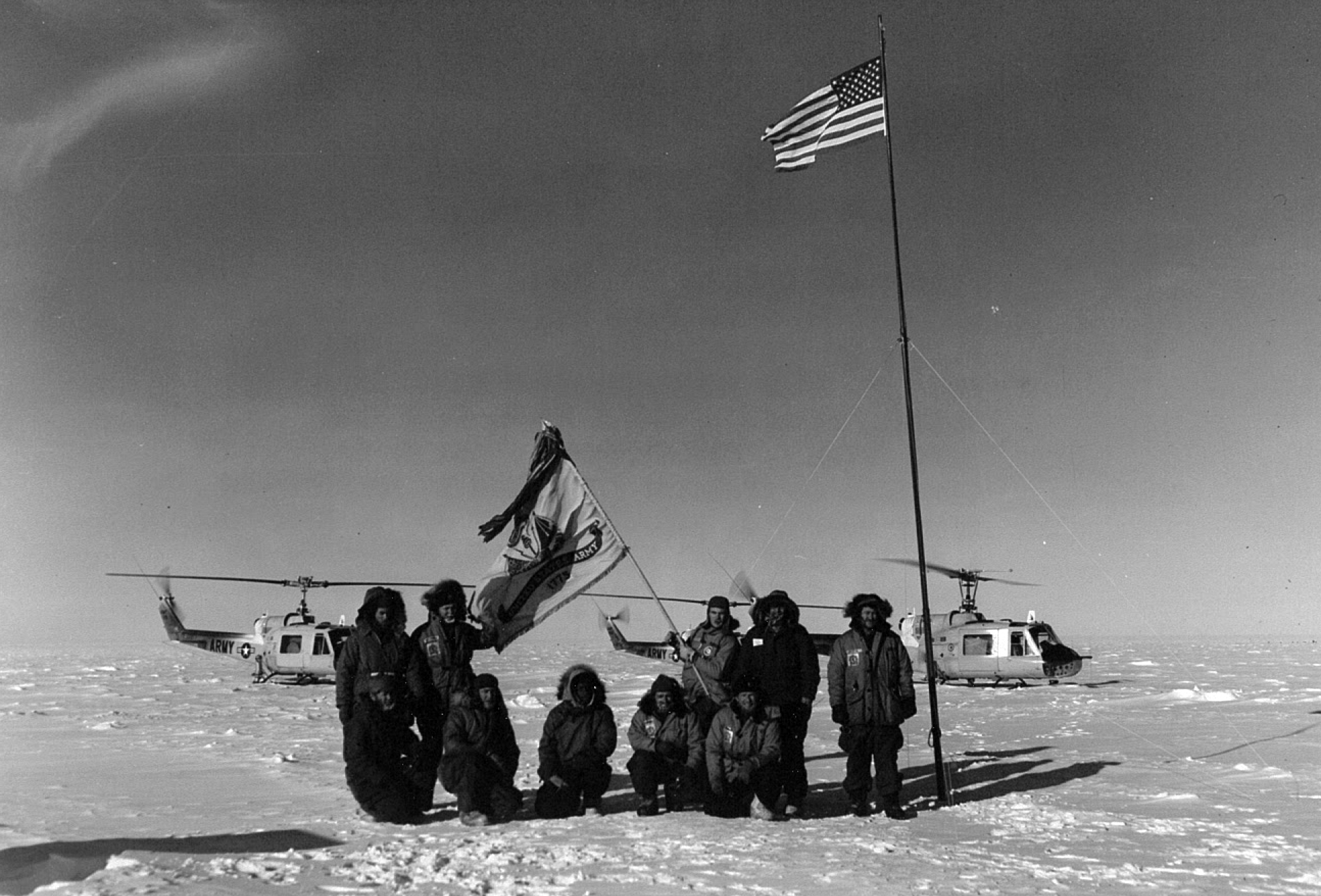 Men stand next to a flagpole on ice.