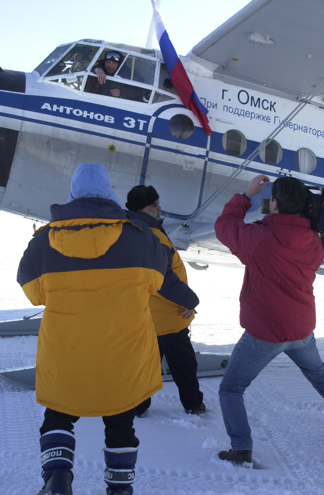 Three people look up at the pilot of a small airplane that is sitting on the ground. 