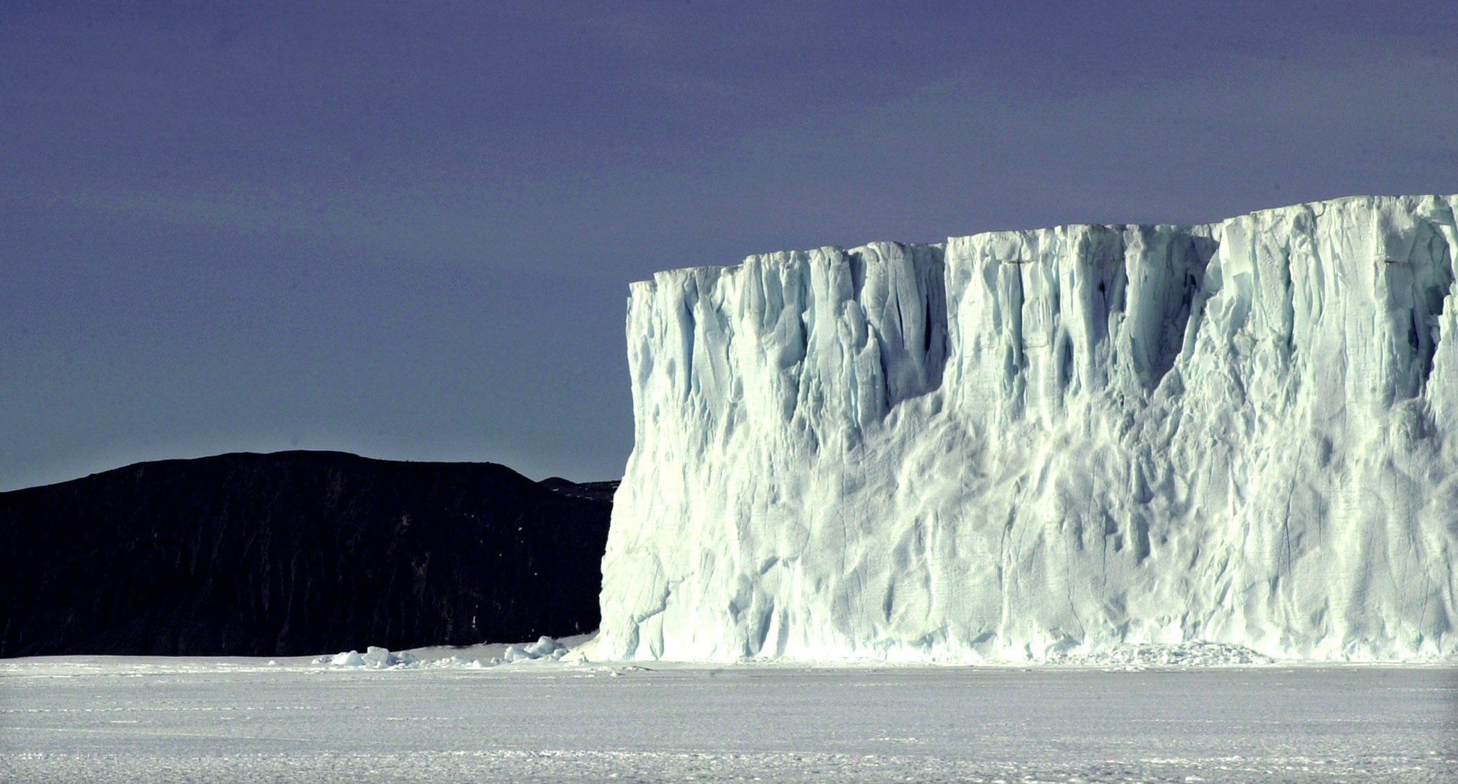 A large glacier extends into a frozen sea.