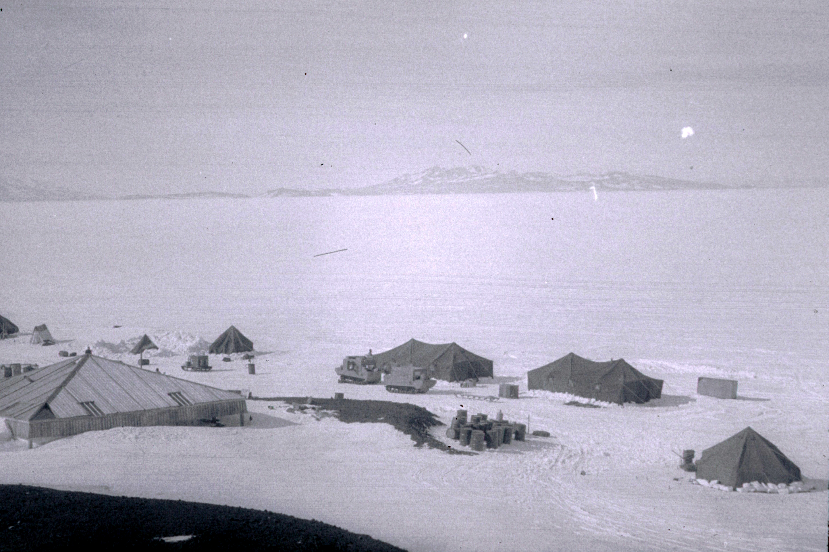 Tents on snow sit near a wooden building. 