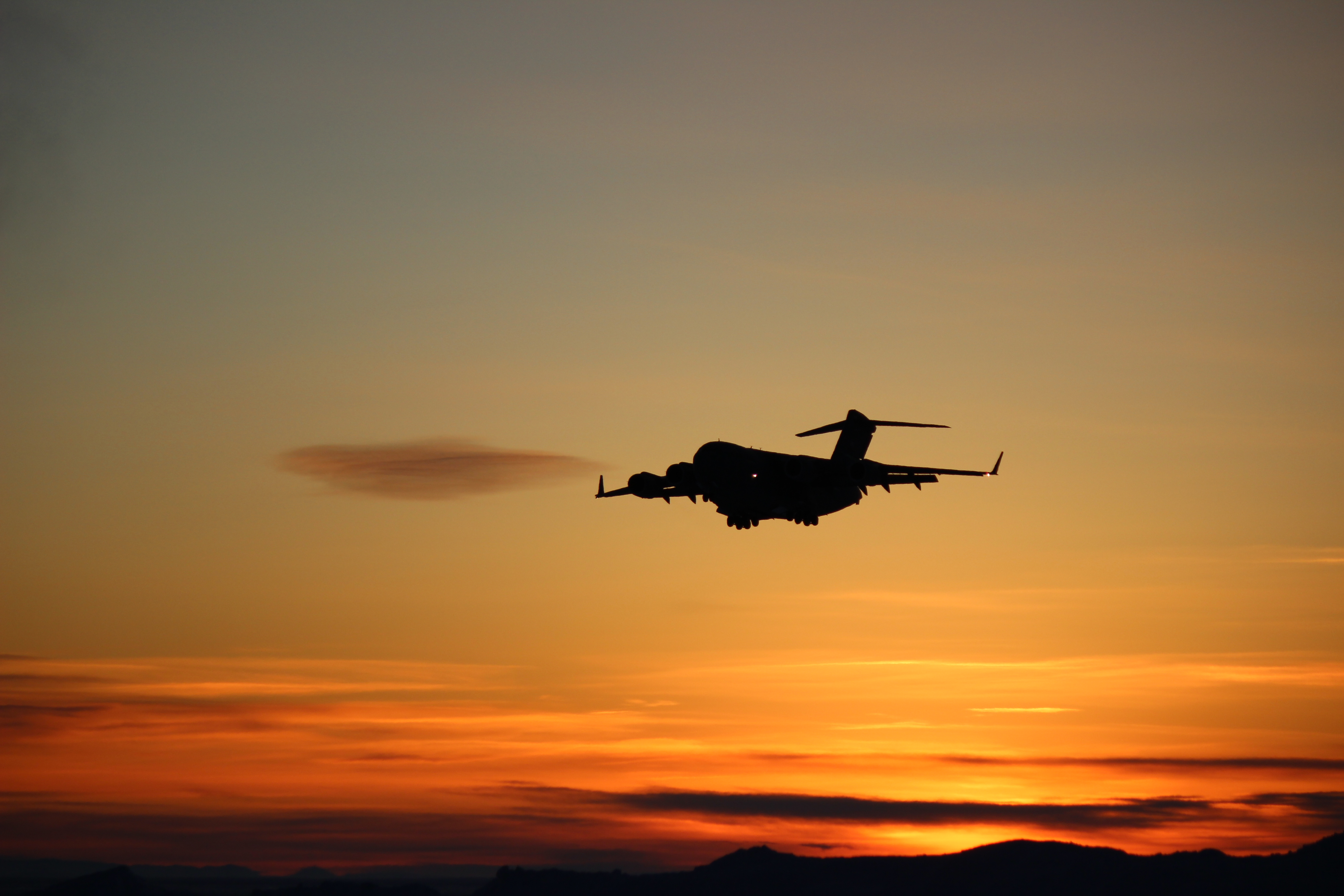 A plane flies across a colorful sunrise.