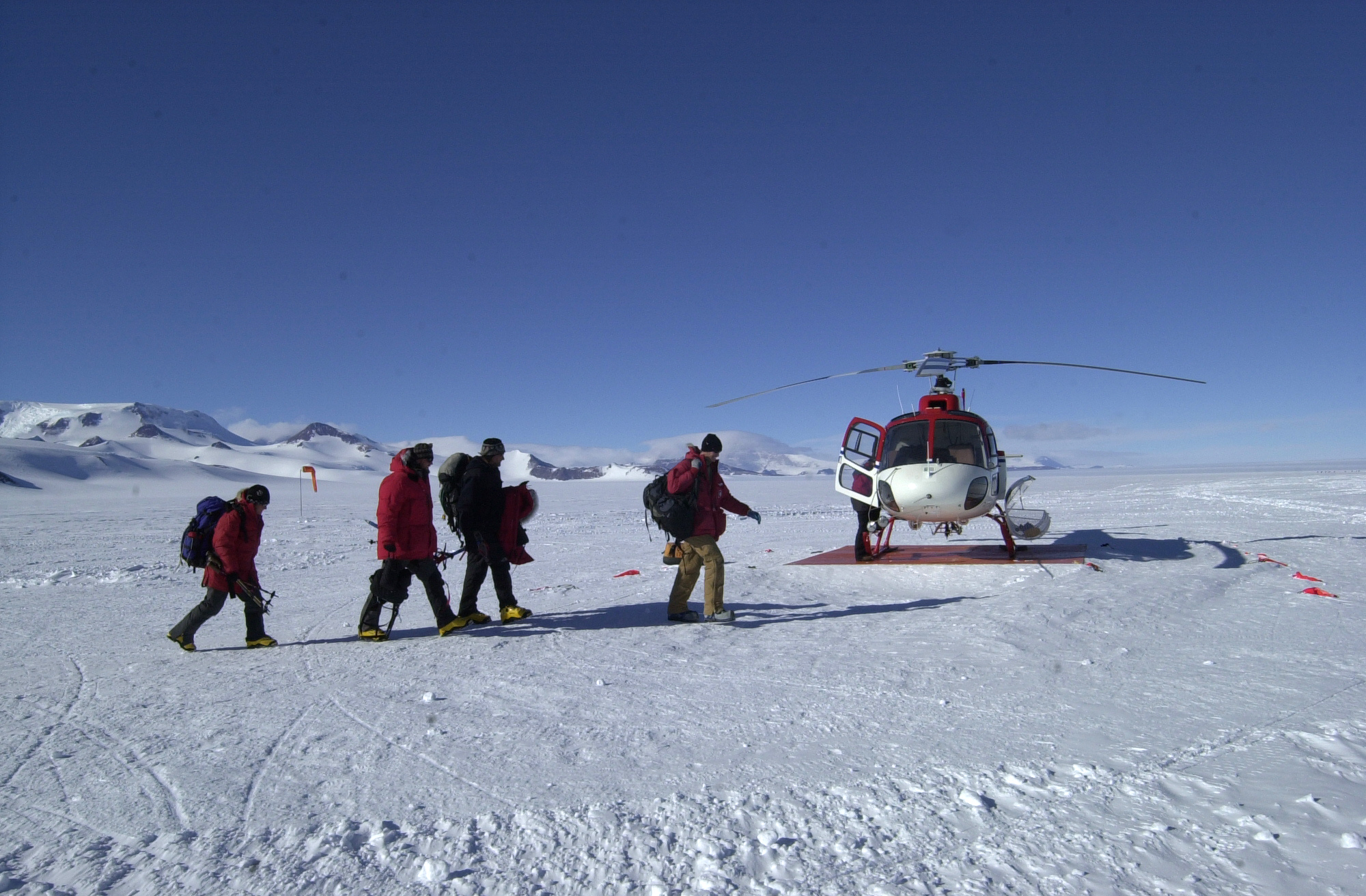 Four men cross snow to a helicopter