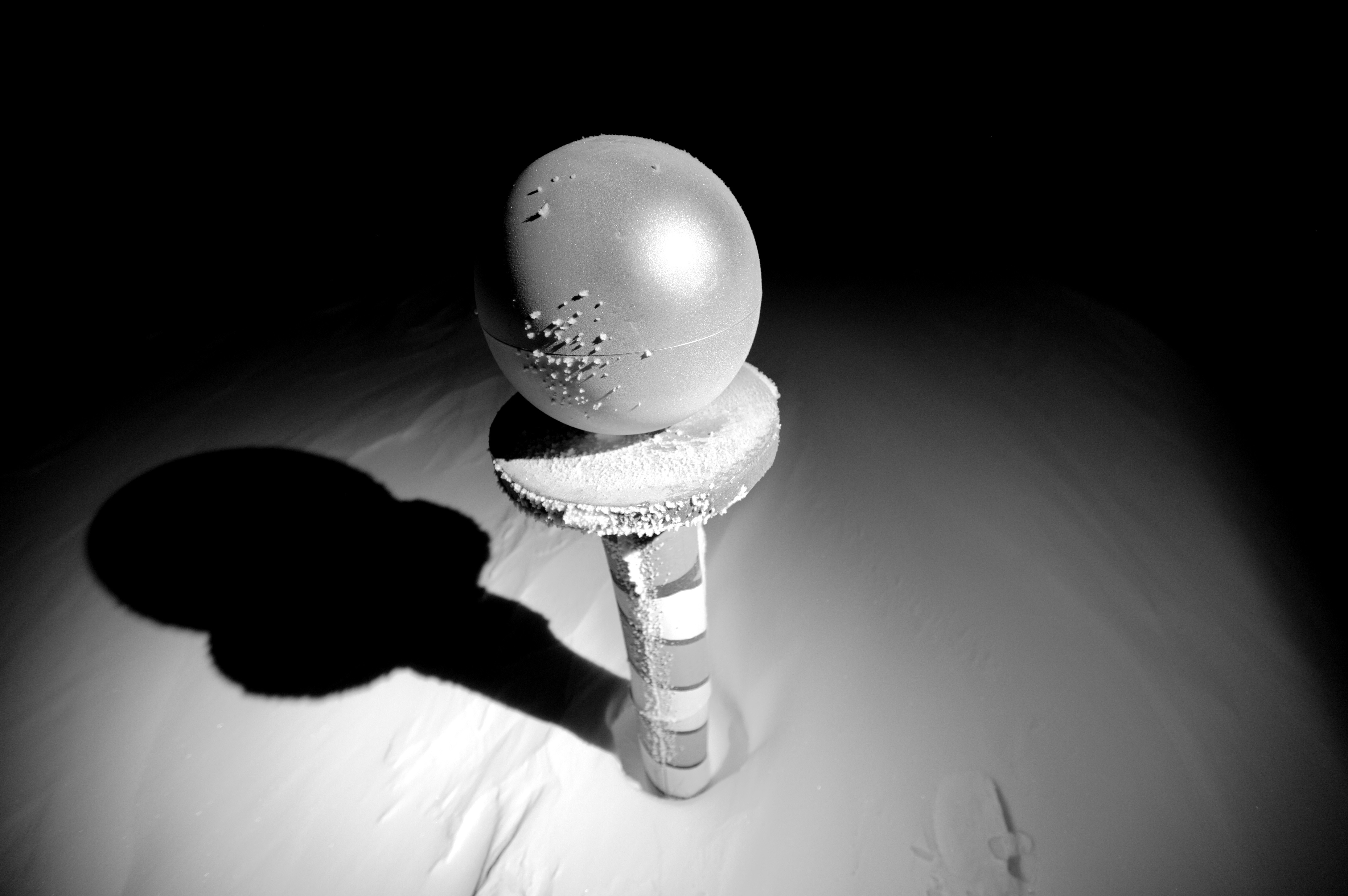 A pole with a sphere on top stands in the snow.