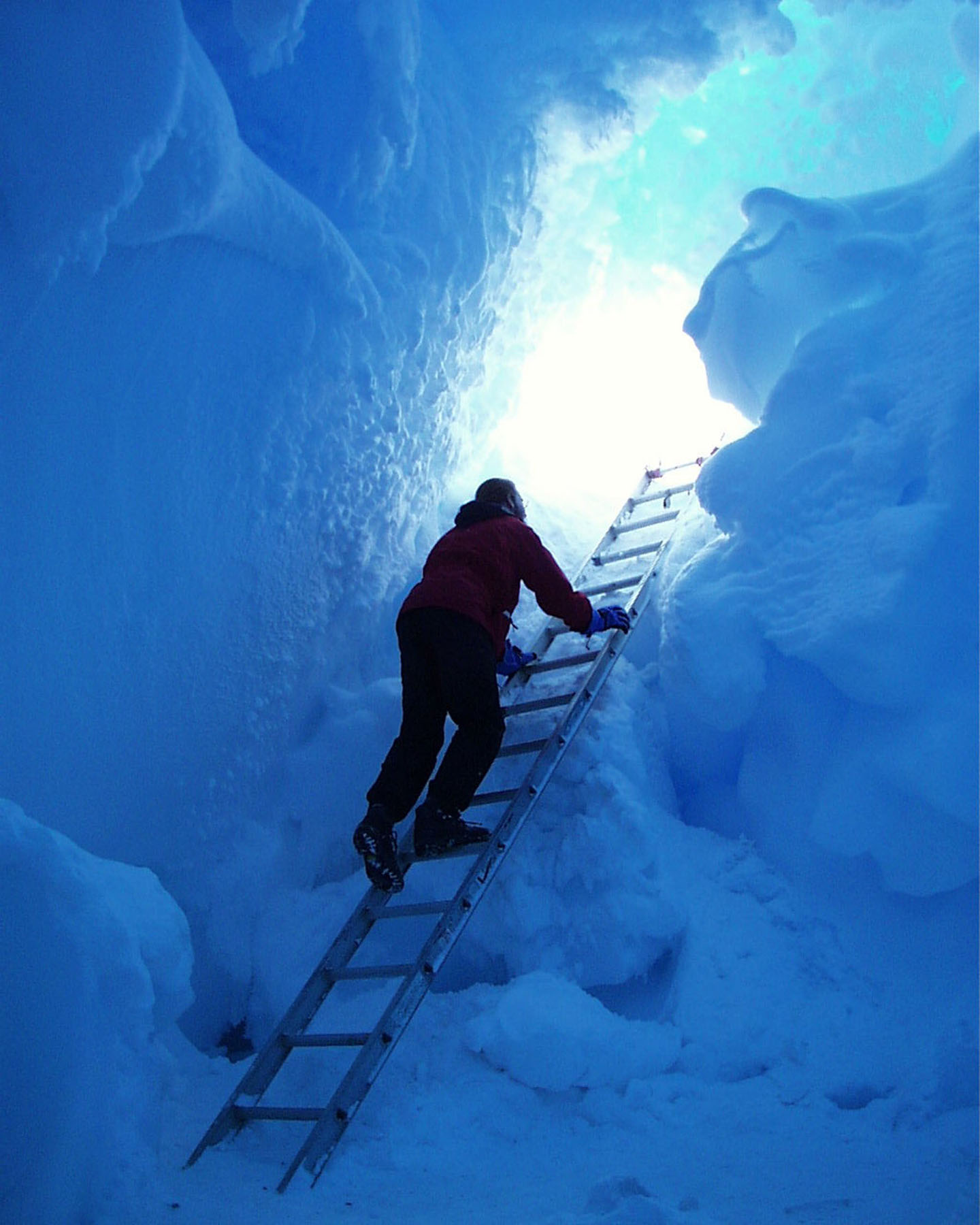 A person on a ladder in a bluish snow cave.