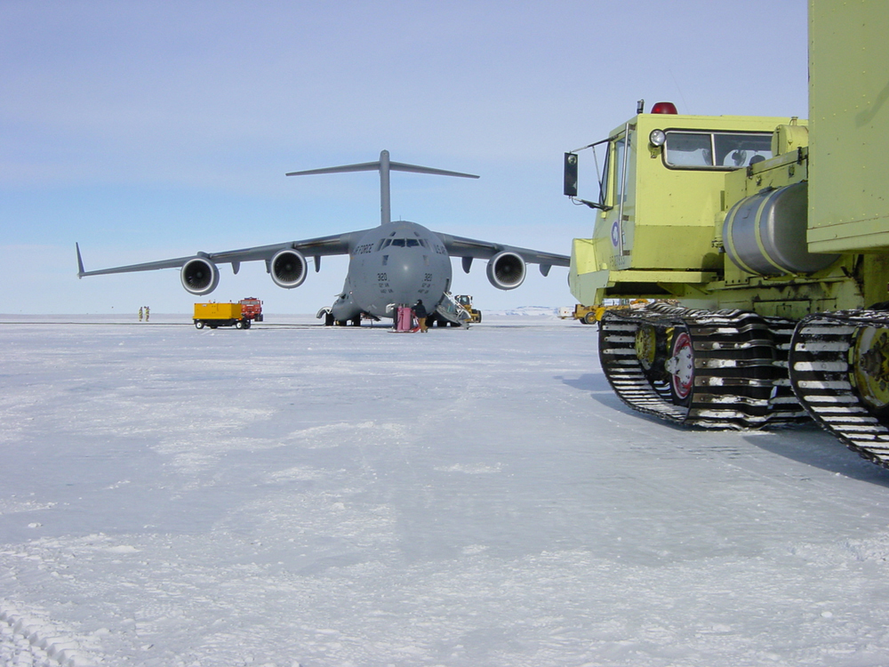 Yellow truck parks near a jet on ice.