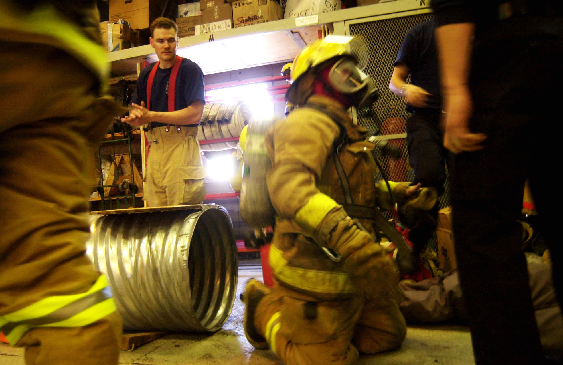 A firefighter emerges from a metal tube-like tunnel.