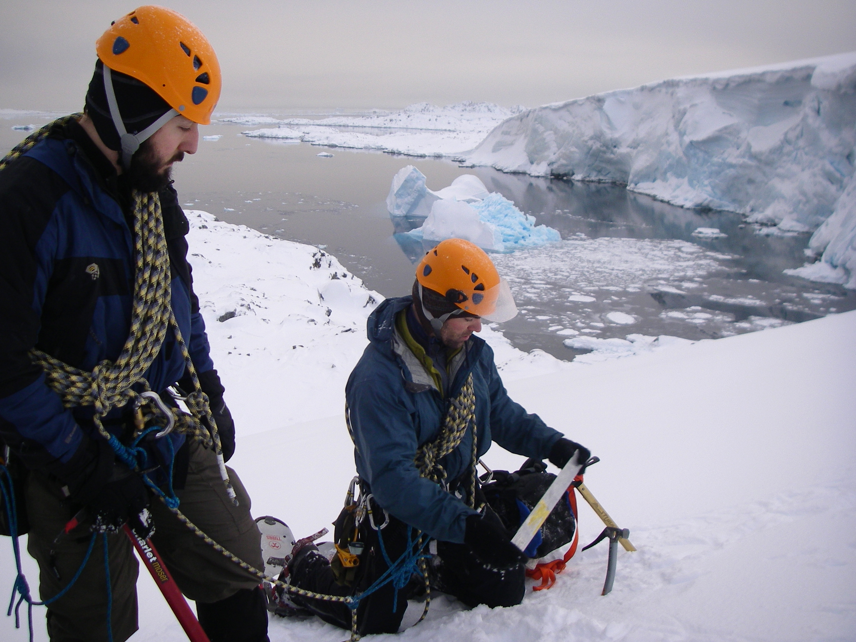 Two men with climbing gear on snow.