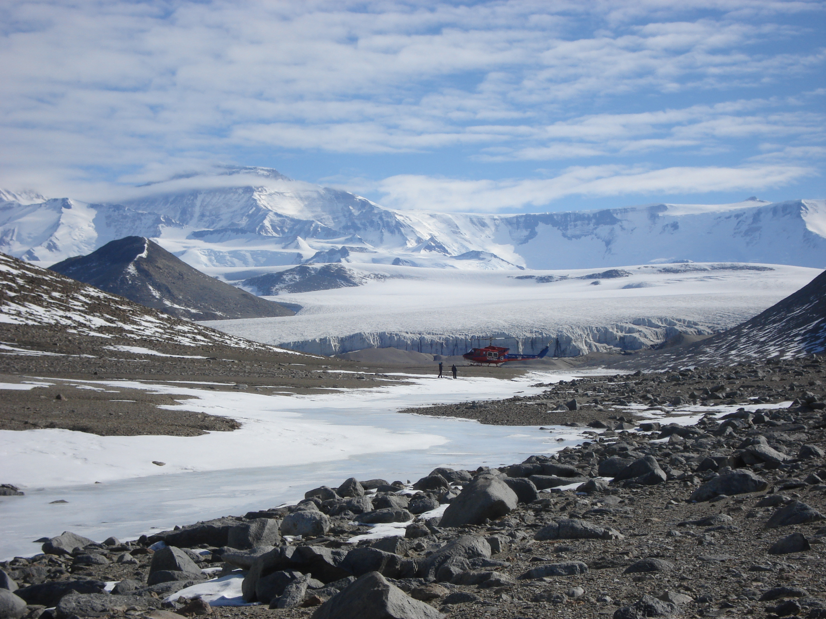 A helicopter and people on the ground near a glacier.
