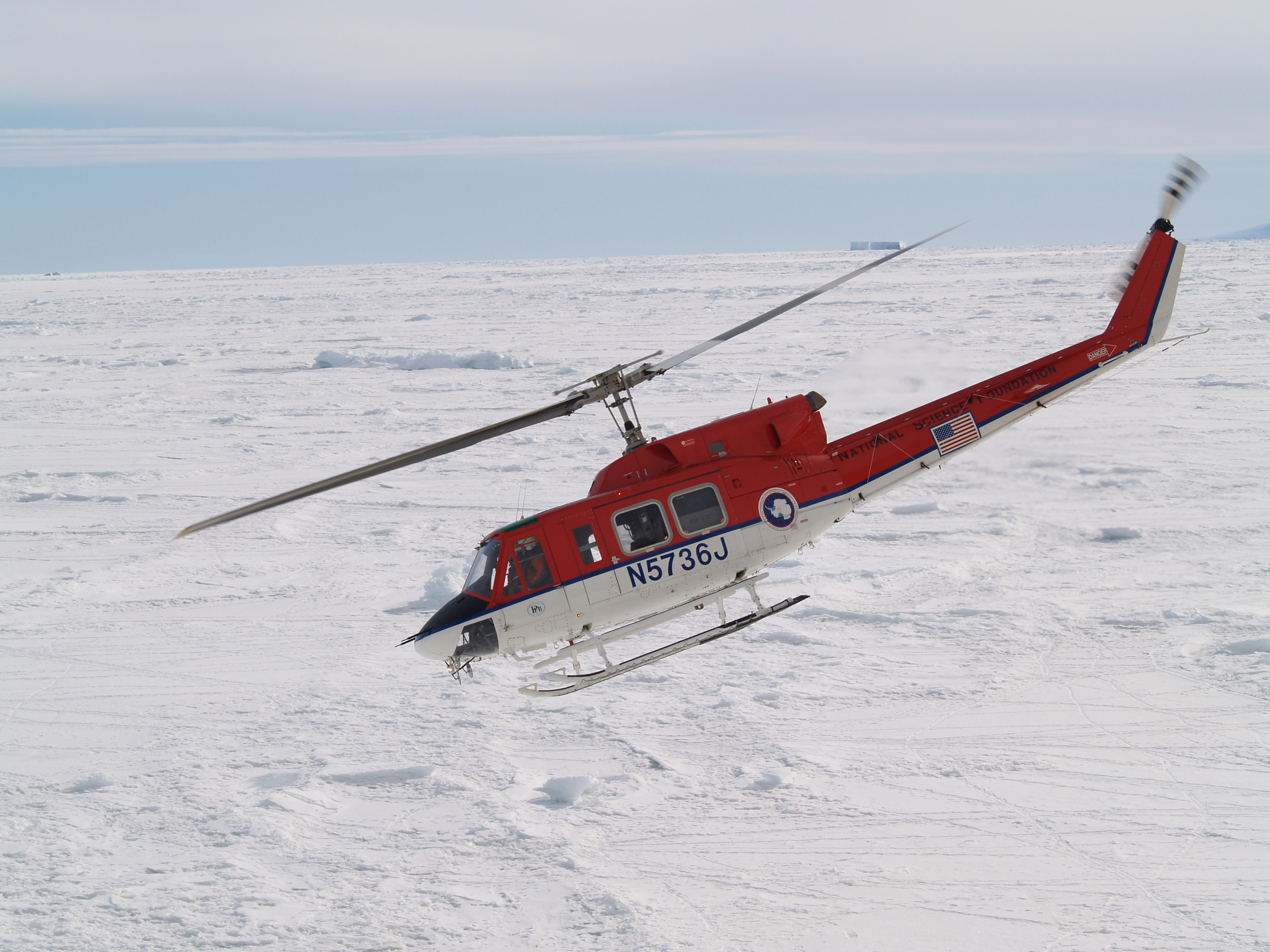A helicopter flies over ice.