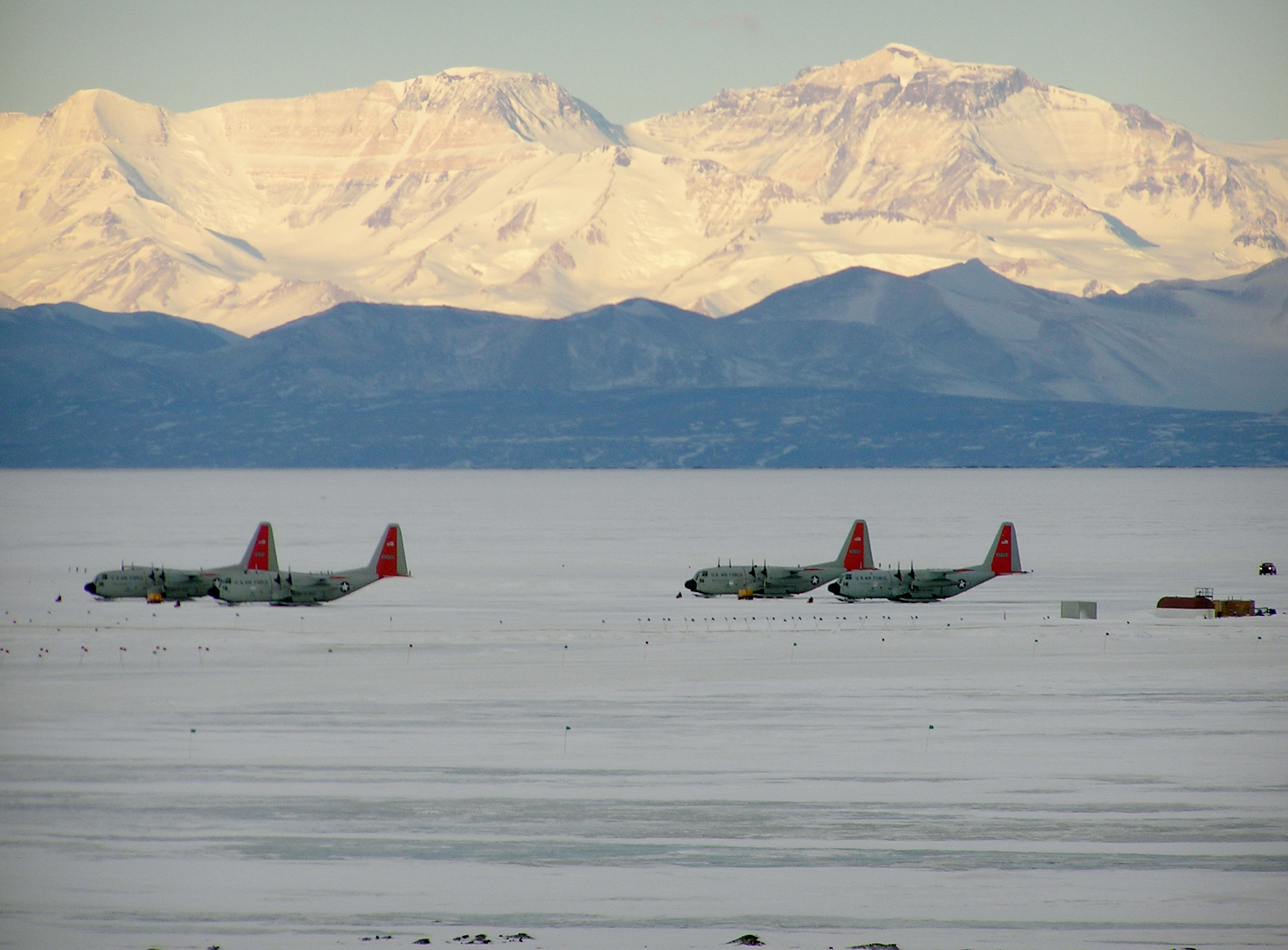 Airplanes sit in front of a glaciated mountain range. 