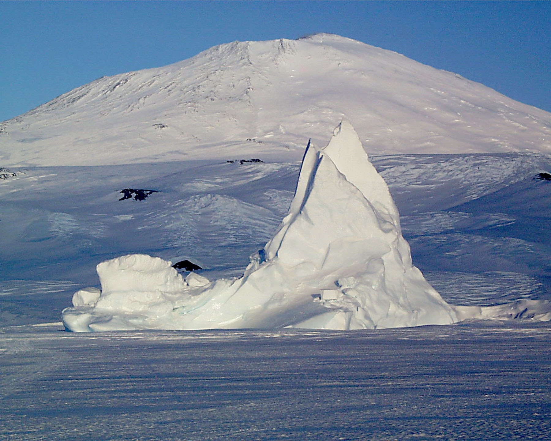 A snow covered mountain in the background and snow and ice in the foreground.