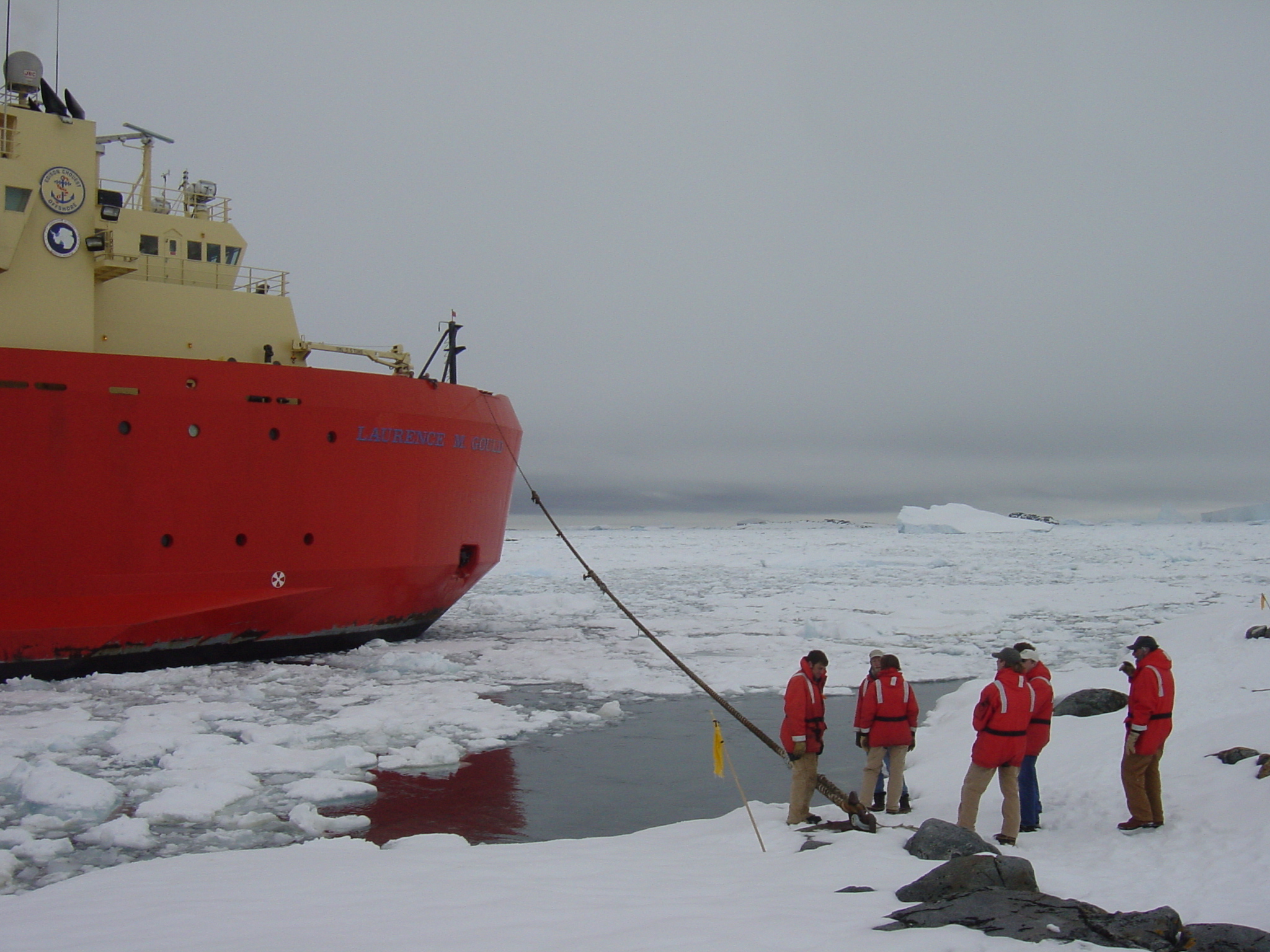 The front side view of a red and yellow ship in icy water.