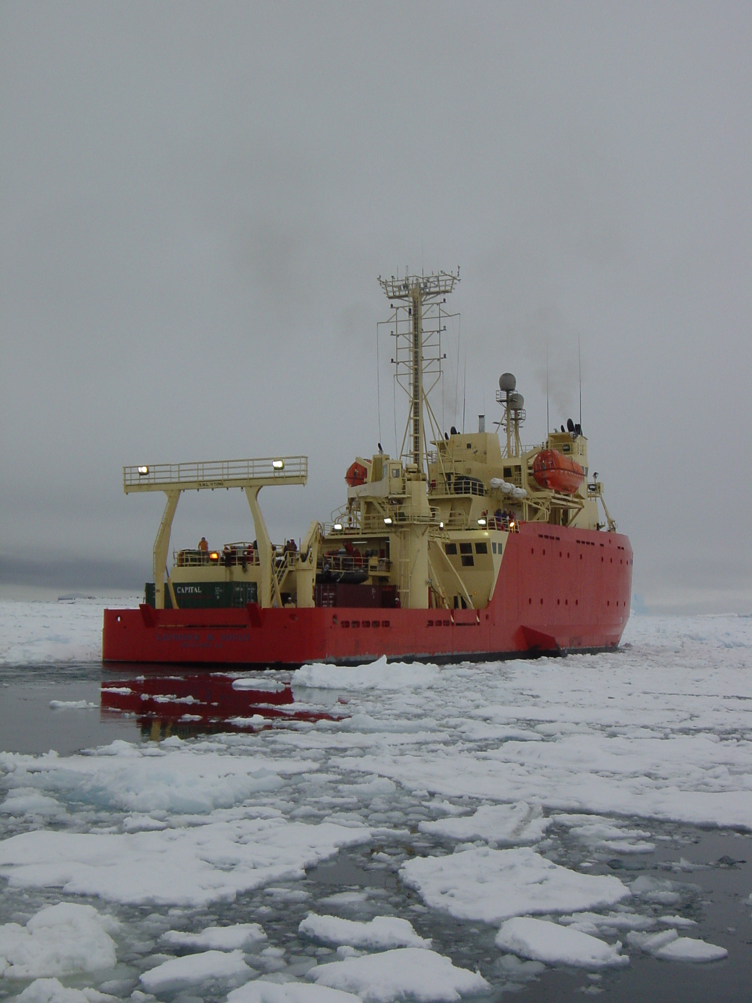The starboard side of a red and yellow ship in icy water.