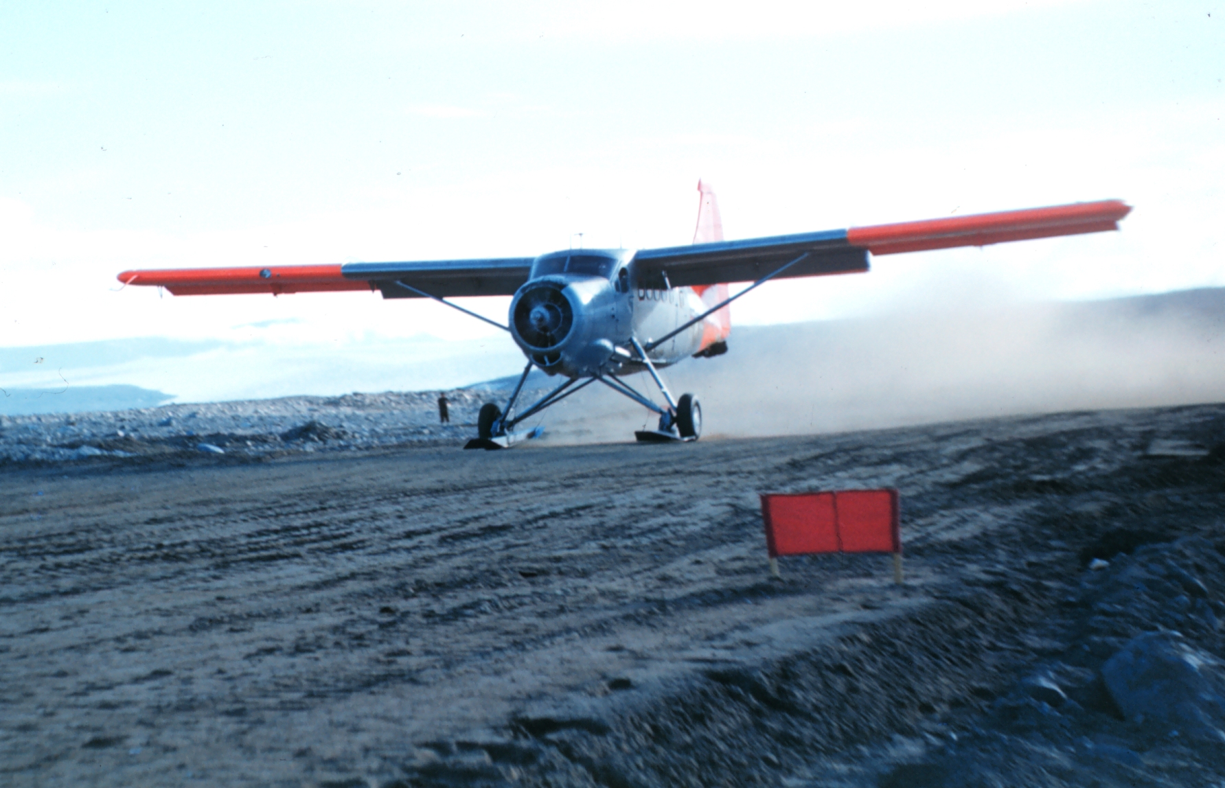 A small airplane lands on a dirt runway.
