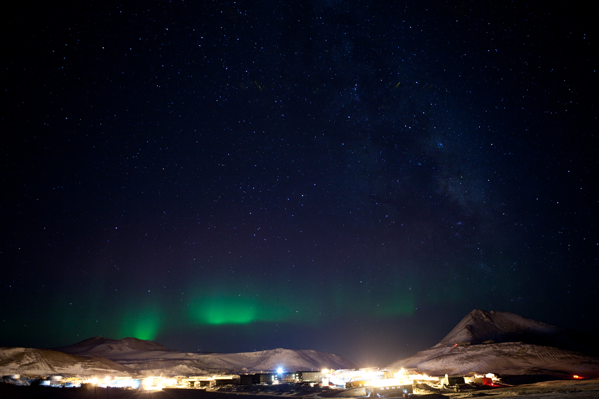 An aurora shines over a brightly lit U.S. research town at night.