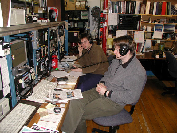 Two men sit at a radio communications panel.