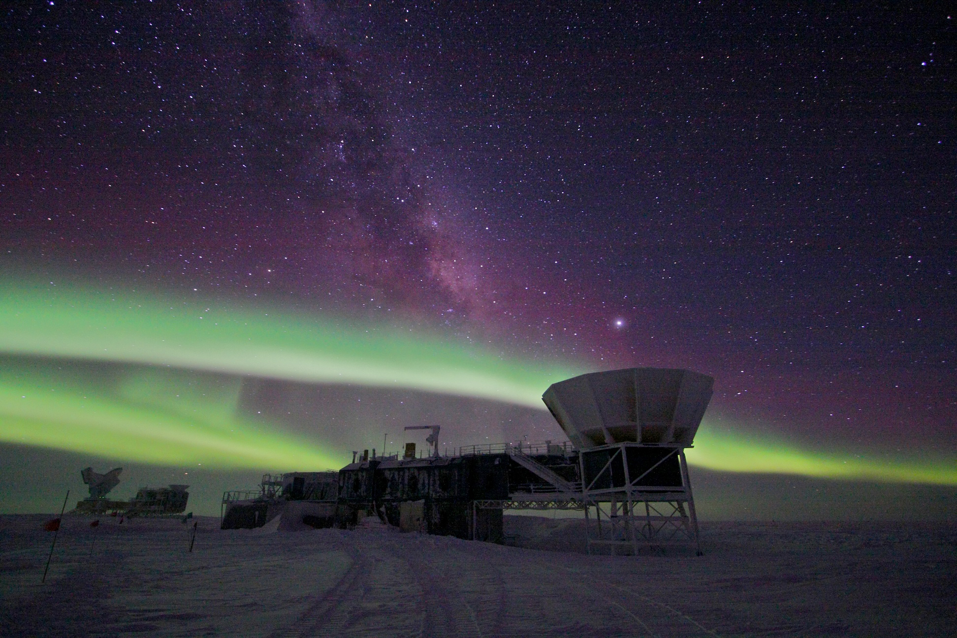 Auroras in the night sky over a science building and telescope at the U.S. research station at the geographic South Pole.