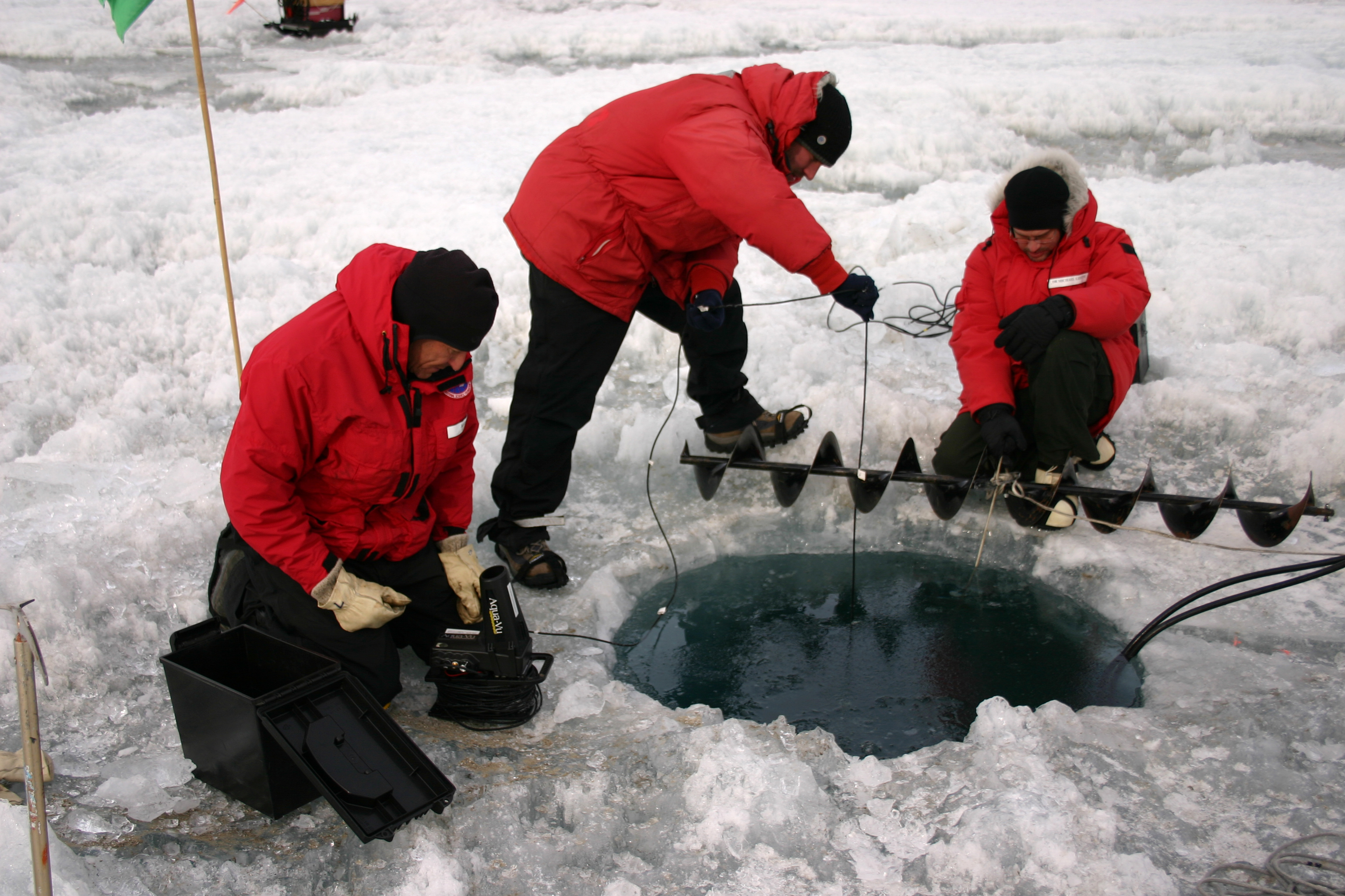 Three men work around a hole in the ice.