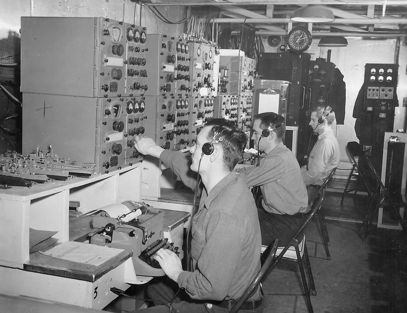 Men sit at radio communications equipment.
