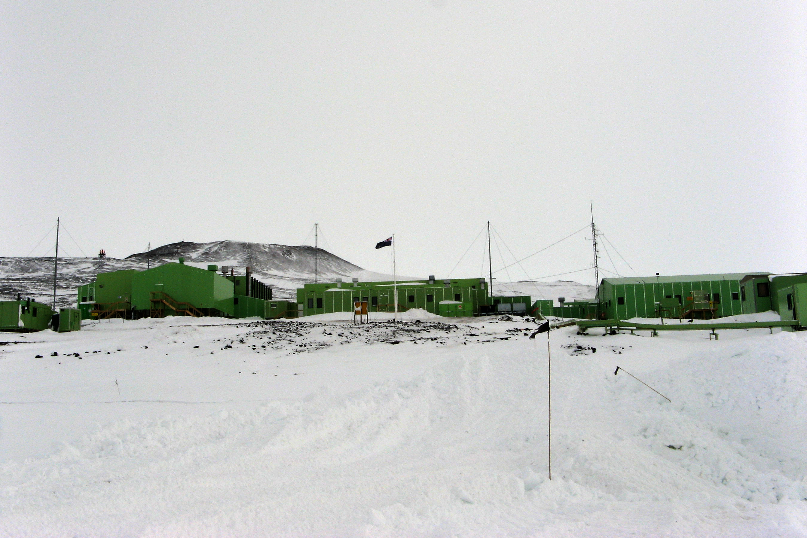 Sheet of ice fronts a cluster of green buildings.