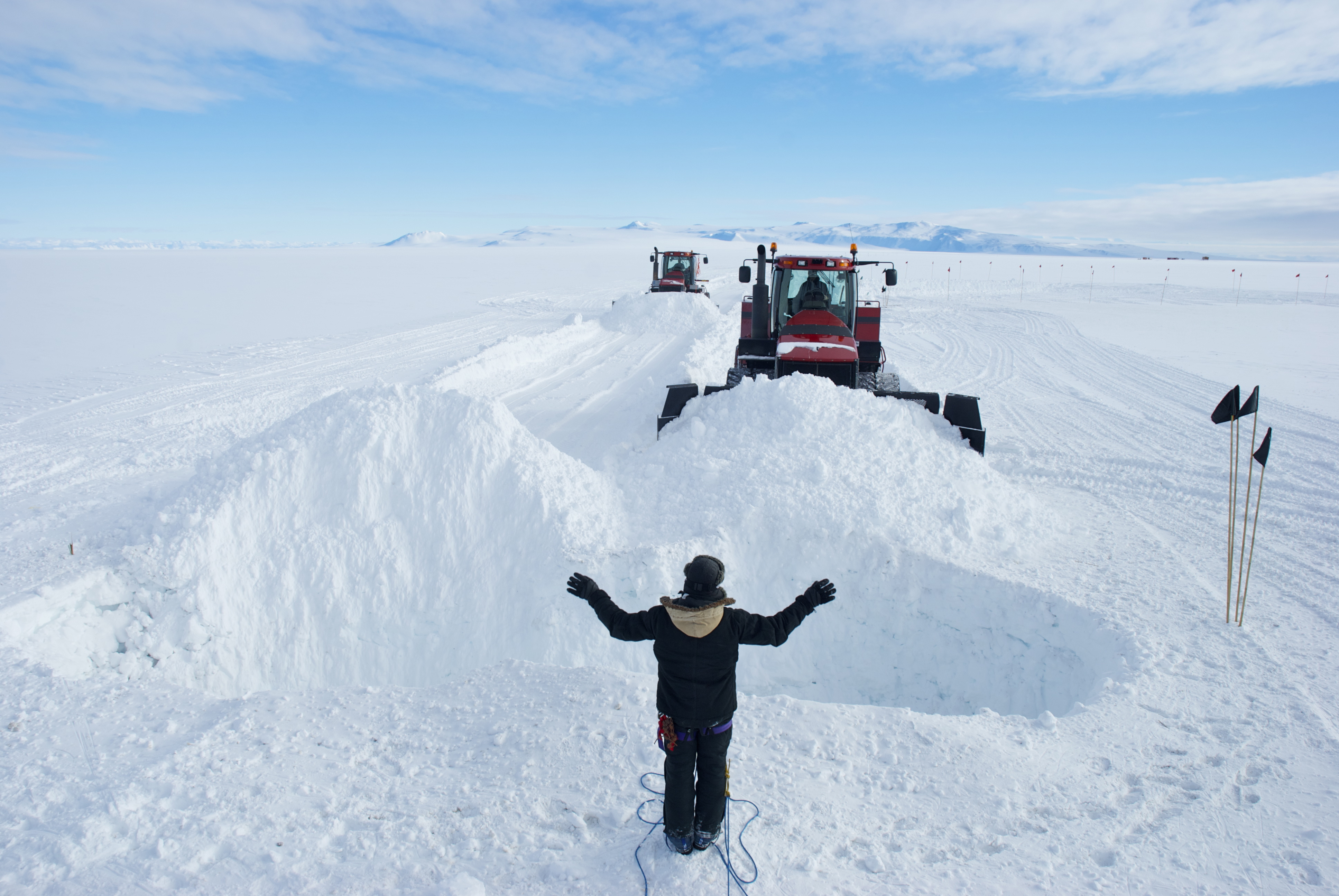 A person guides a tractor pushing snow into a crevasse.