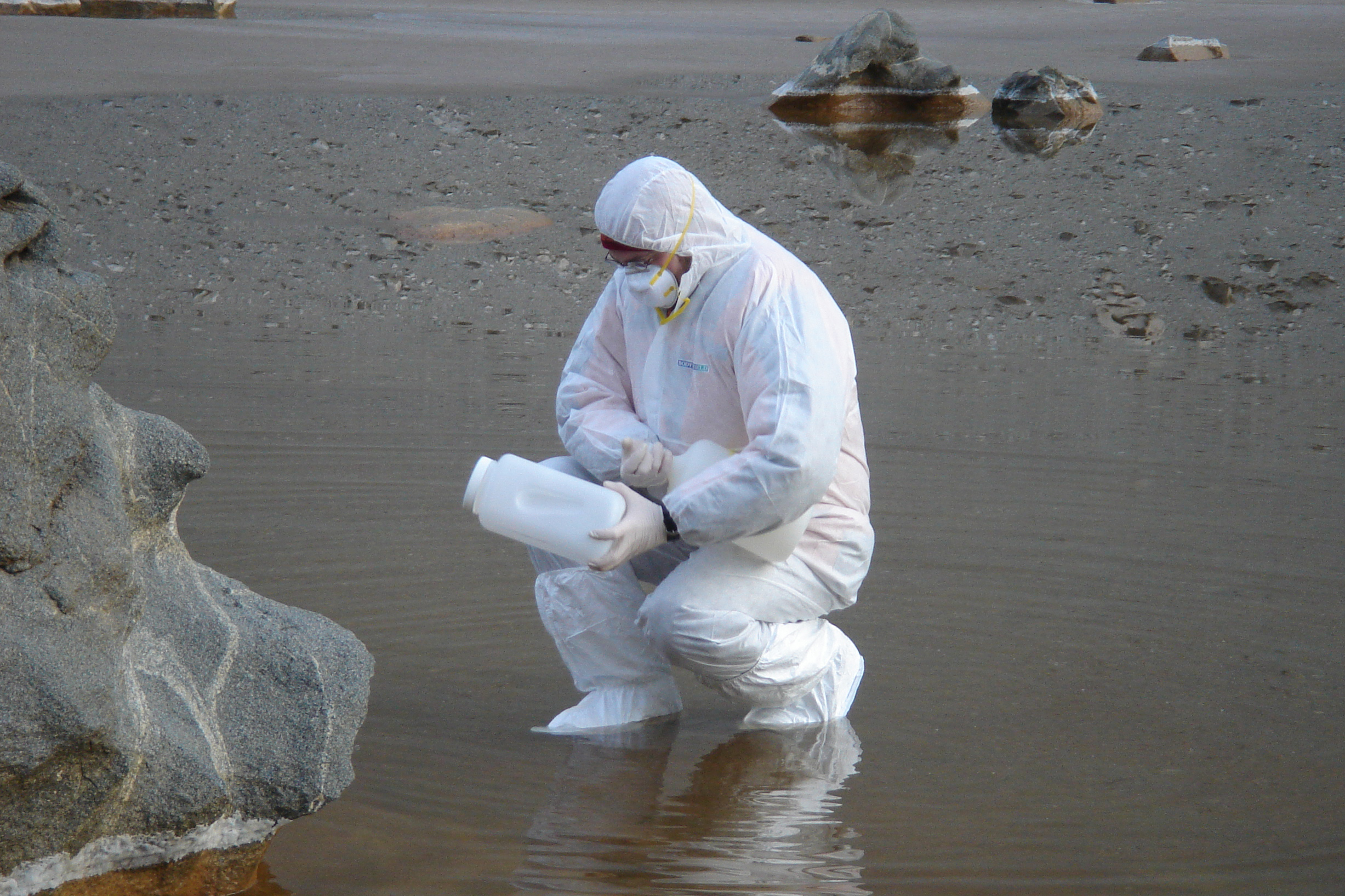 Man in white protective clothing works in shallow water.