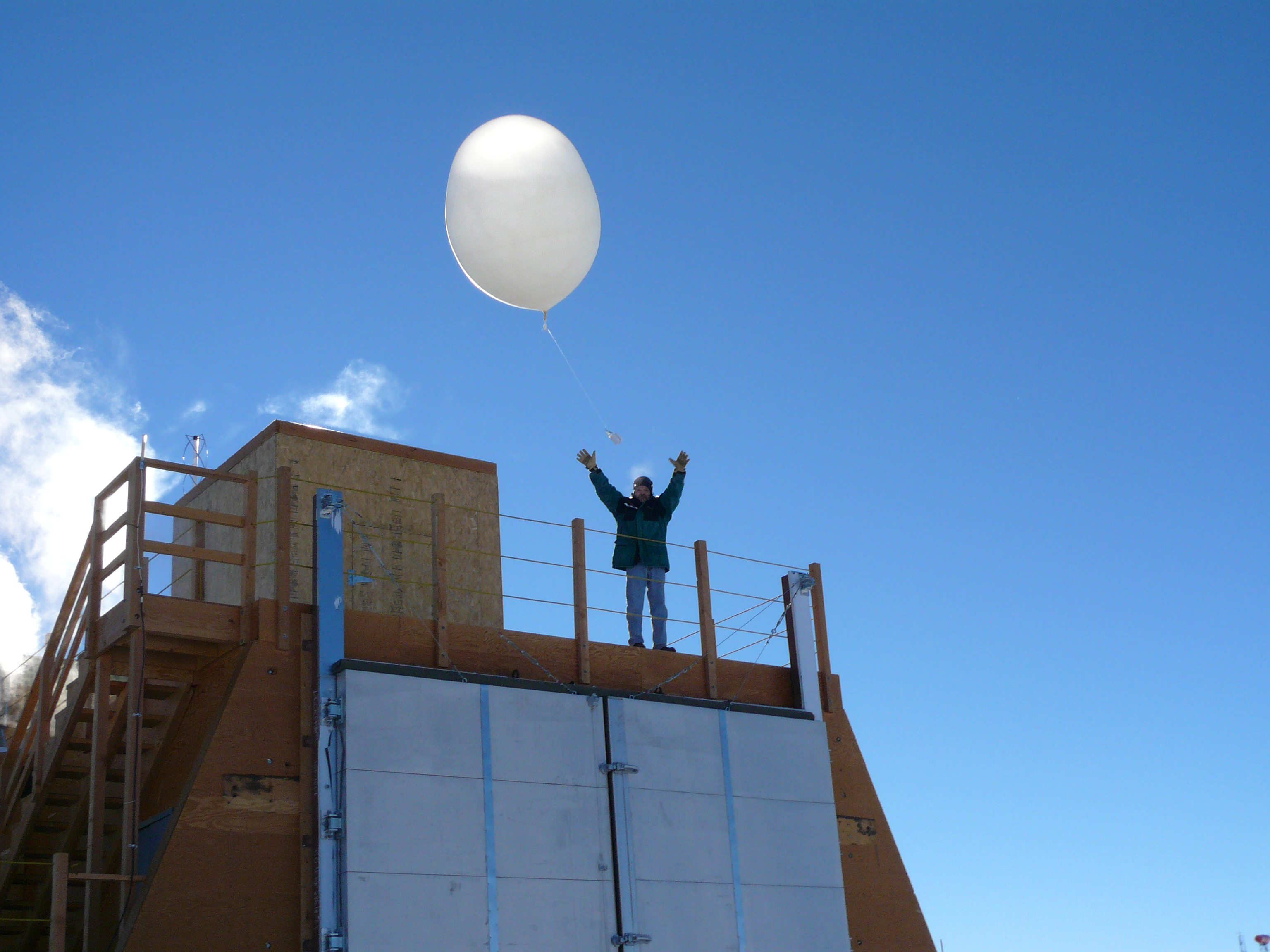 A person releases a large balloon into the air from the top of a building.