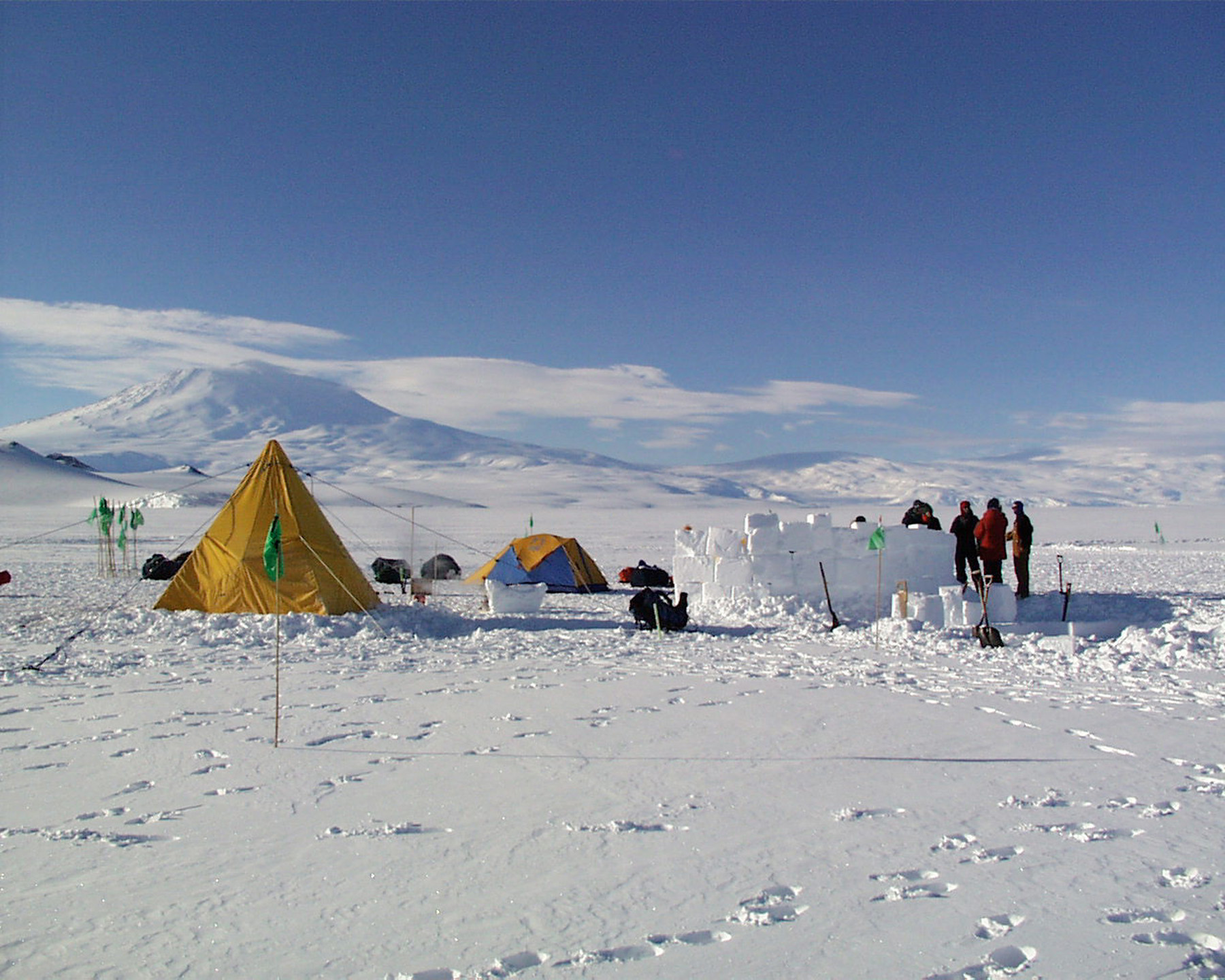 A snow camp with yellow tent and a wall built of blocks of snow.