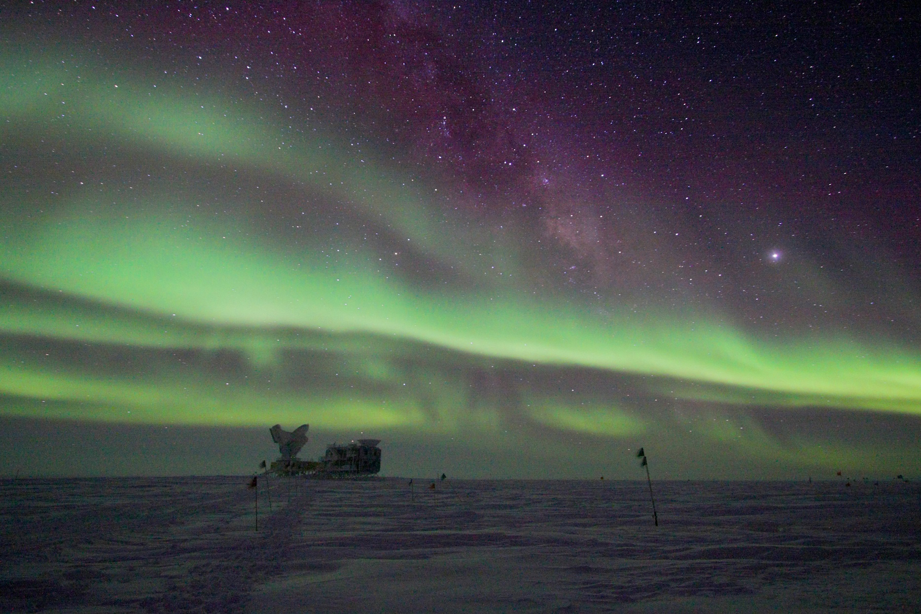 Auroras in the night sky over a science facility at the South Pole.