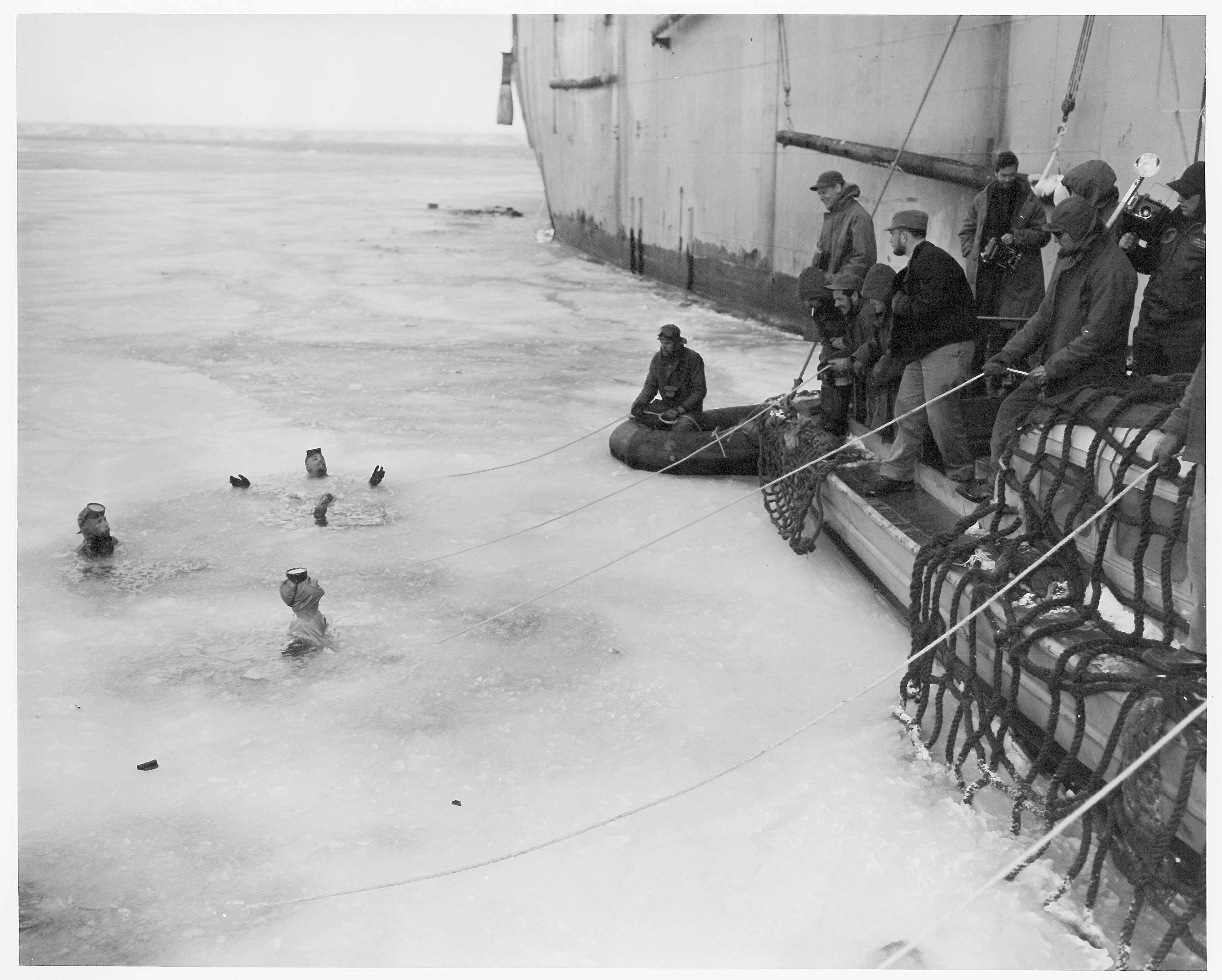 Three men swimming in icy water as several men on a boat watch.