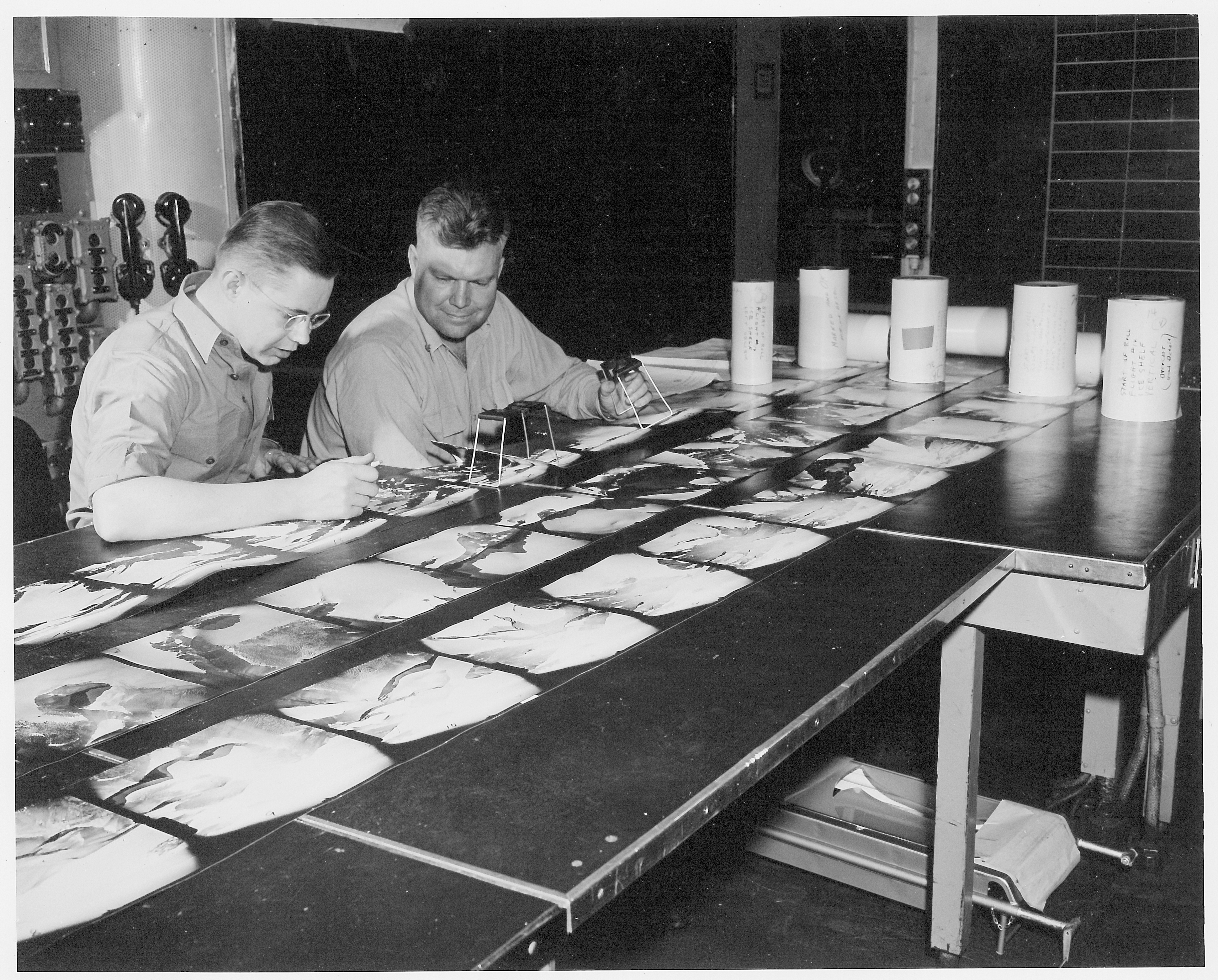 Two men studying photos laid out on a table.