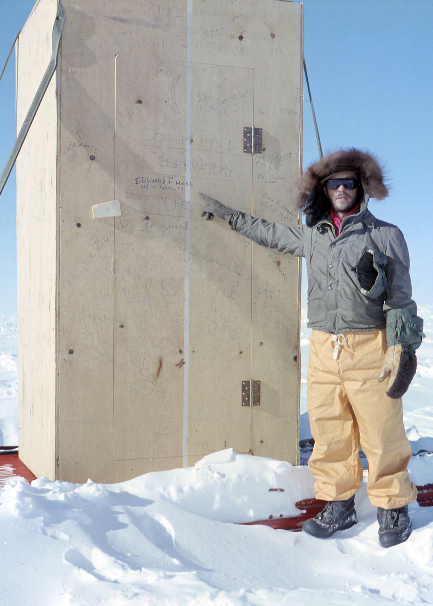 A man outside standing next to a small wooden structure.