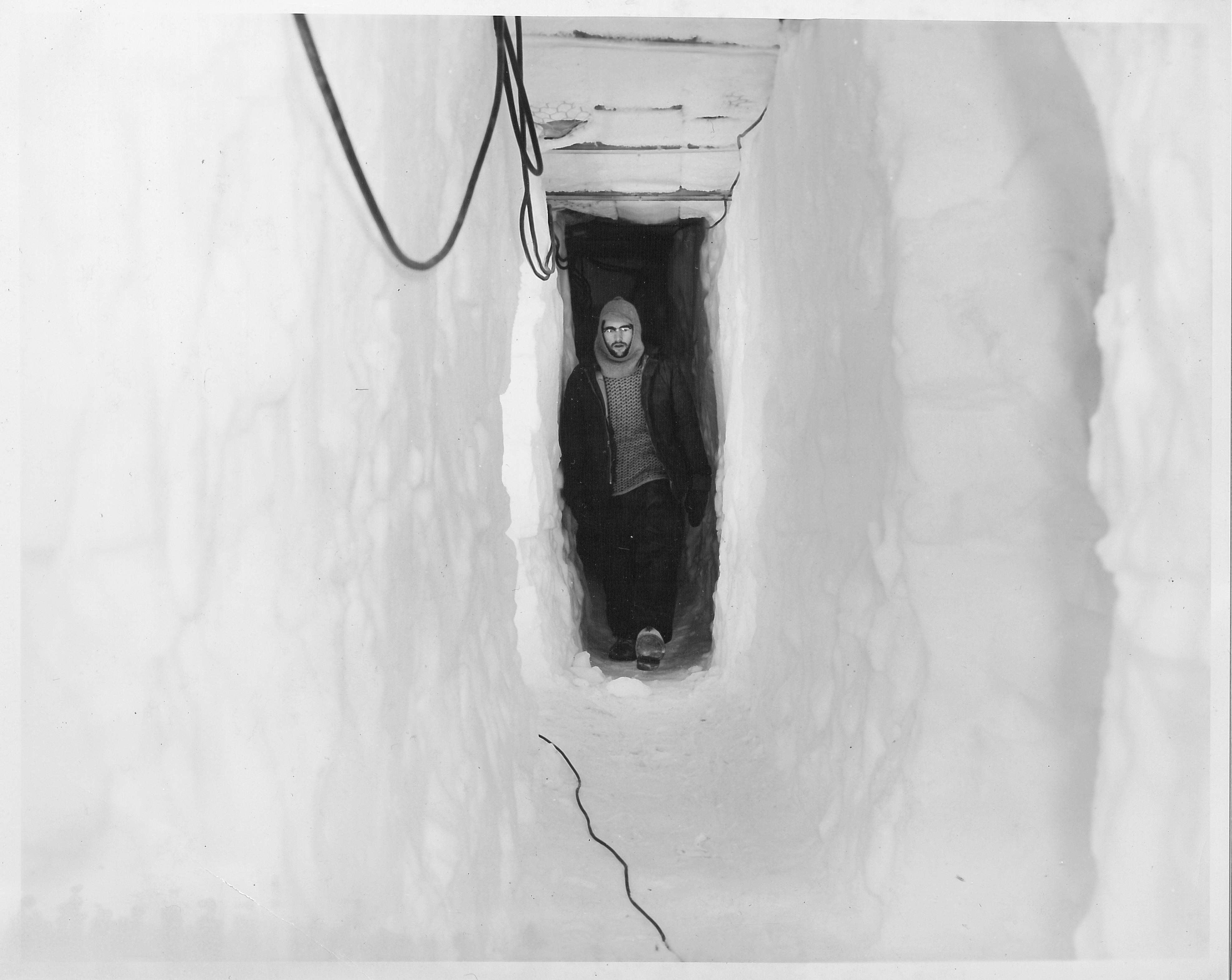 A man walking down a narrow tunnel inside the snow.