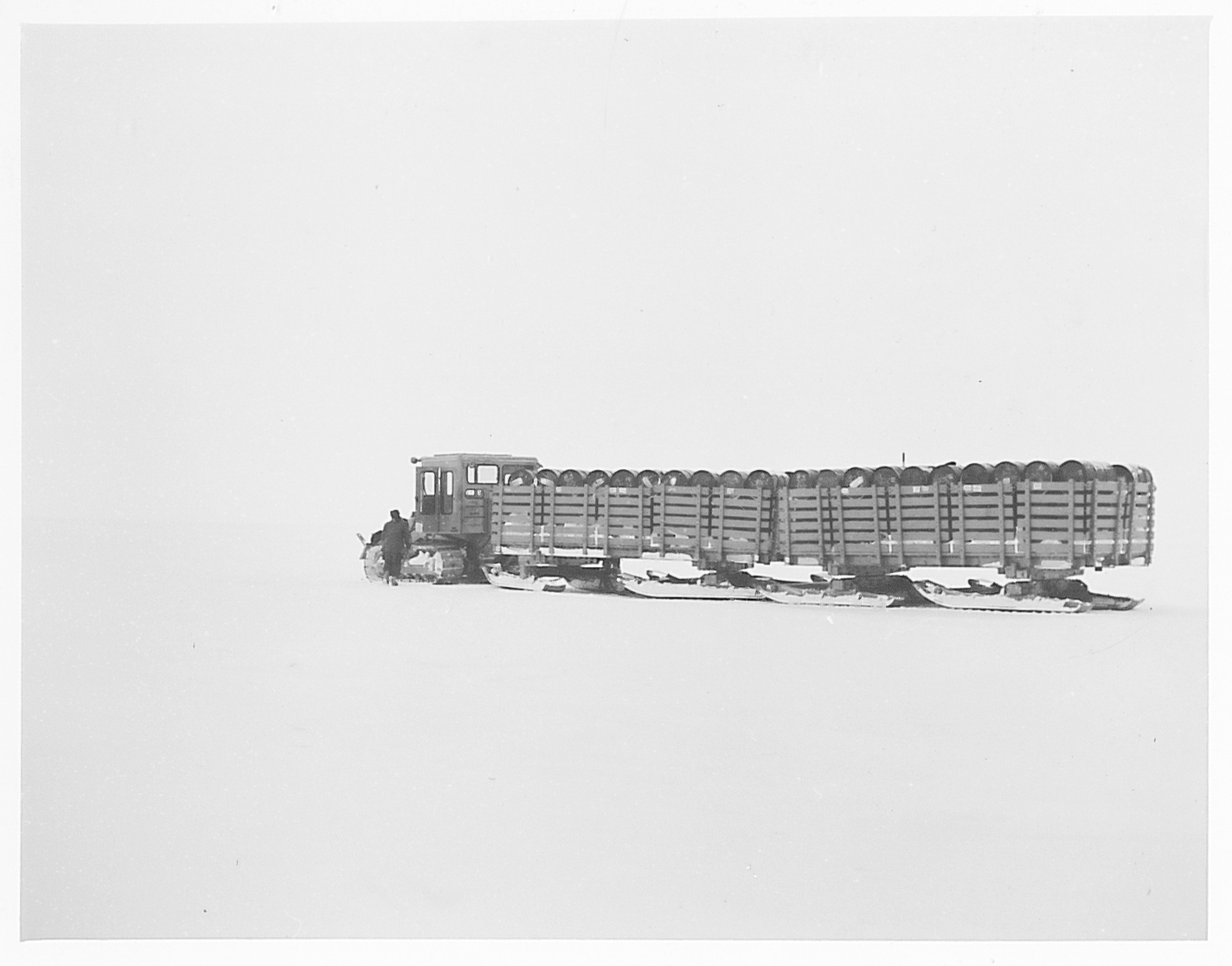 A tractor hauling fuel drums on frozen terrain.