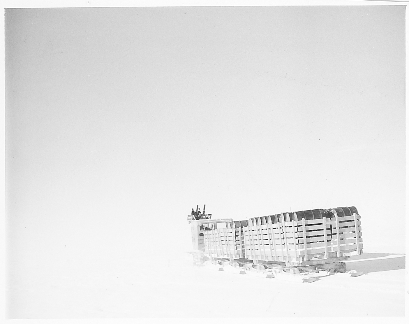 A tractor hauling fuel drums on the snow.