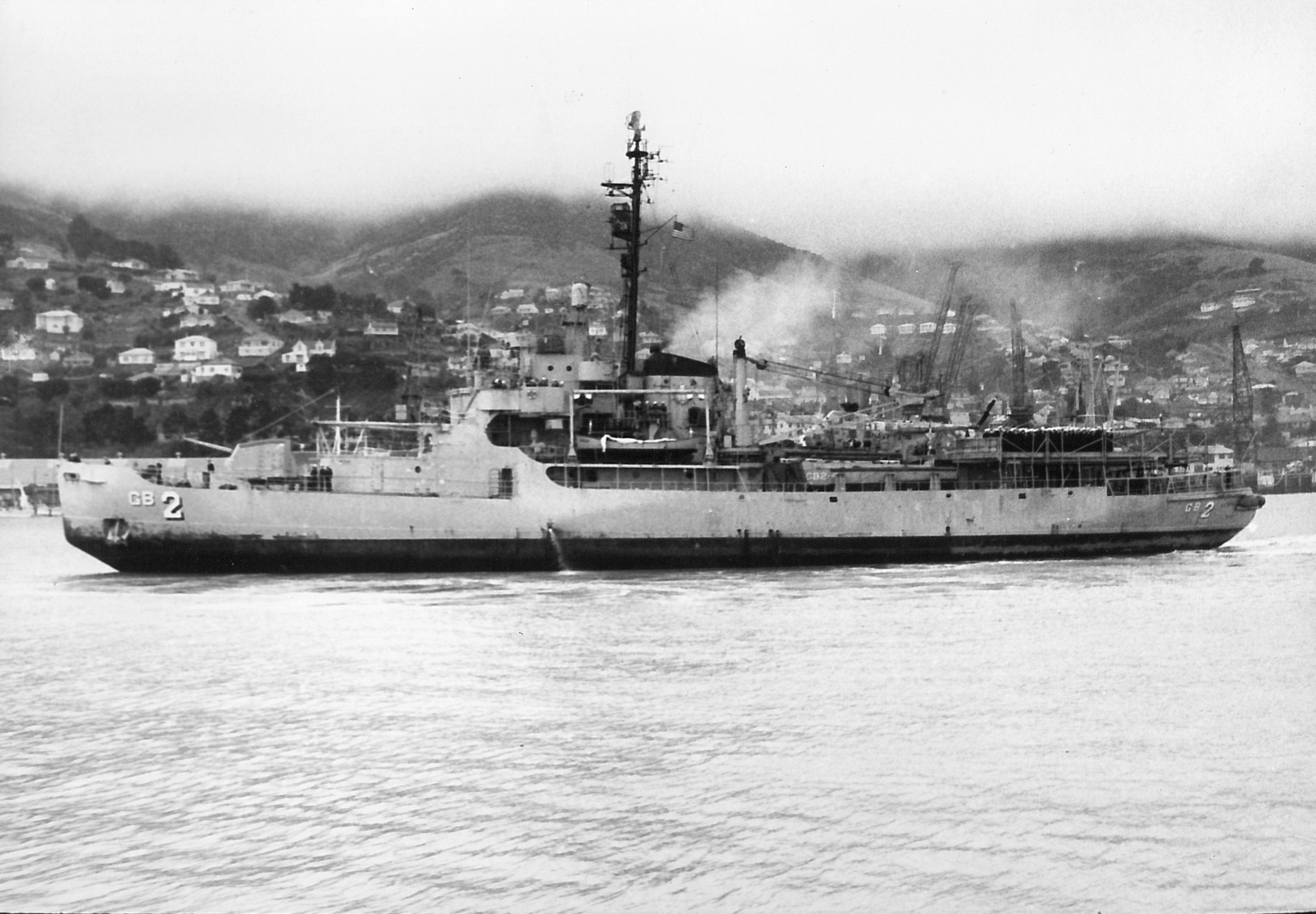 Side view of a ship in the water with mountains in the background.