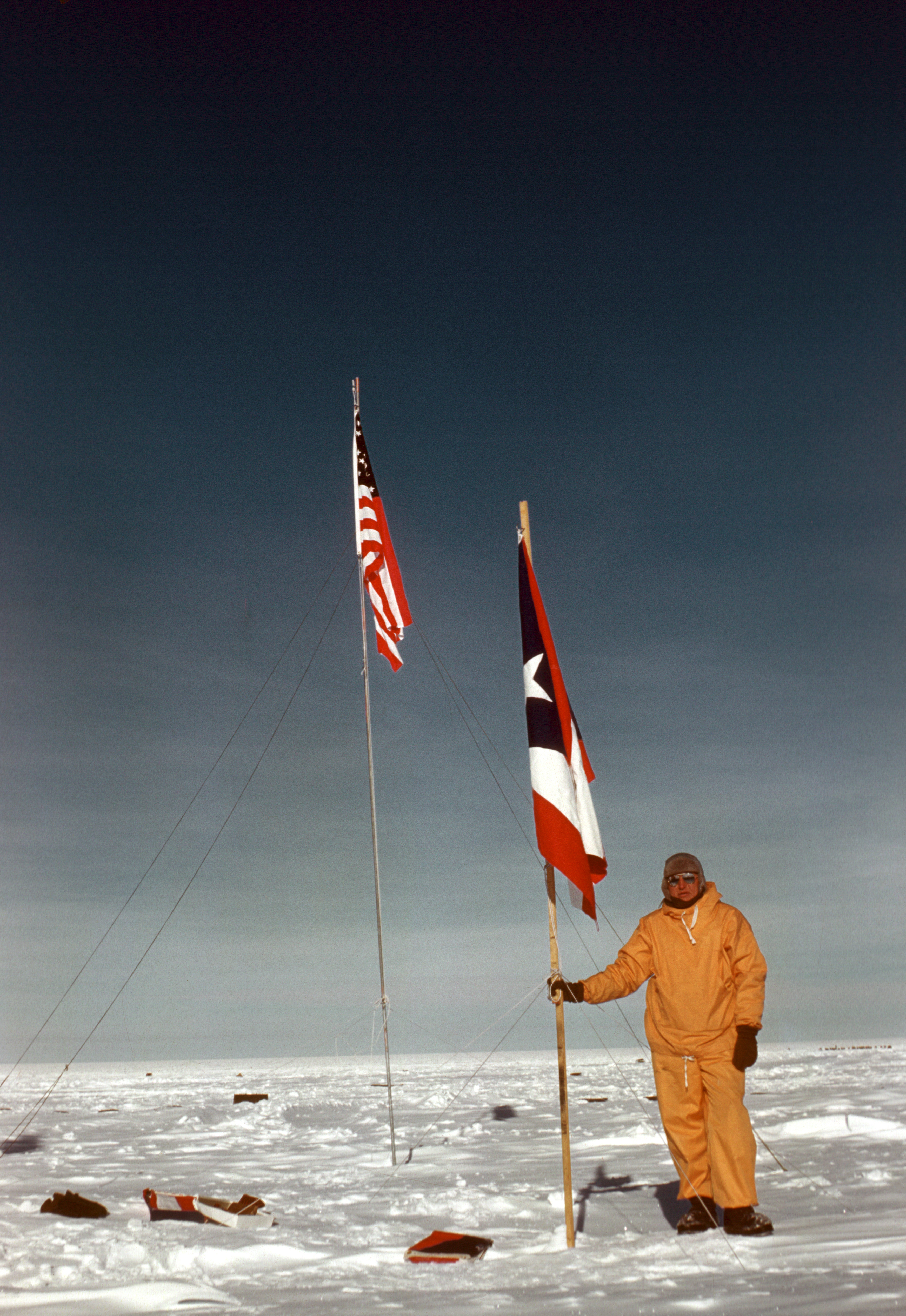 A person standing on a flat snowy surface next to two flags.