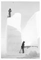 Two men in the snow. One of them standing on a very tall ridge.