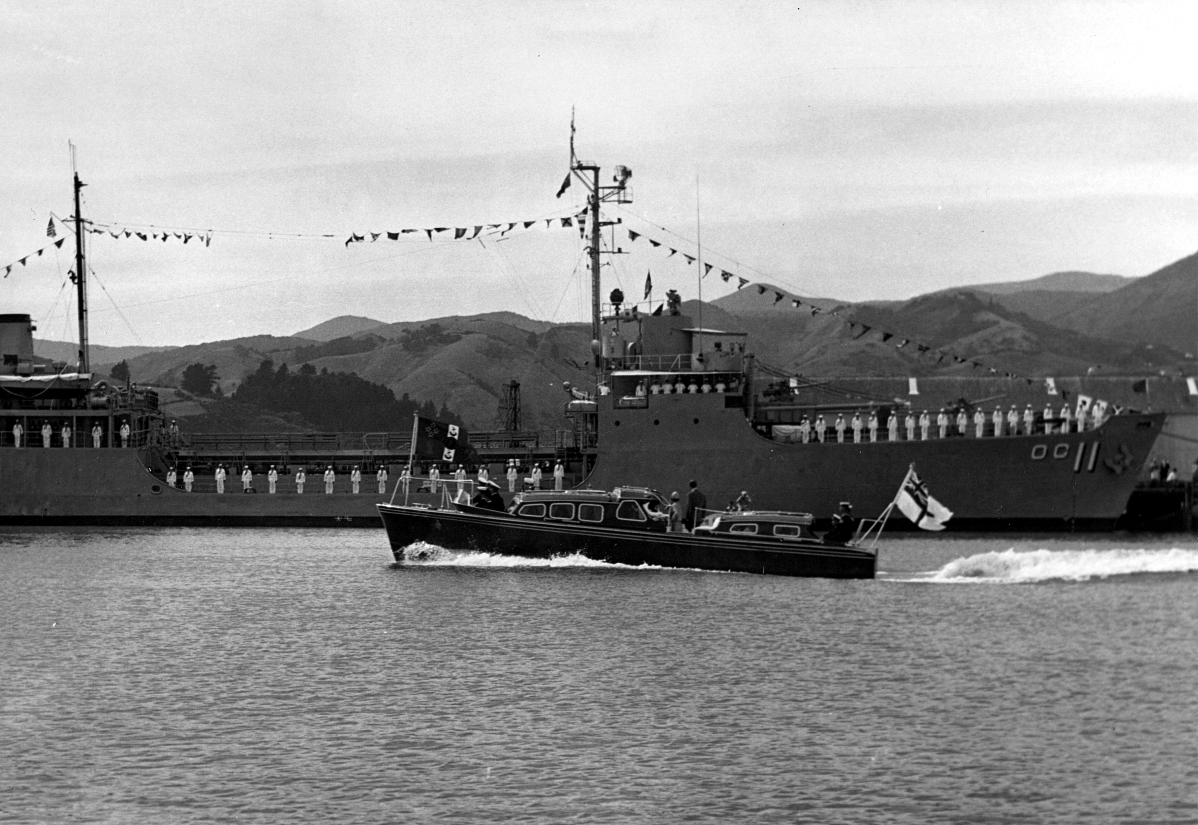 Men on board a U.S. Navy vessel stand at attention while a smaller boat passes by.