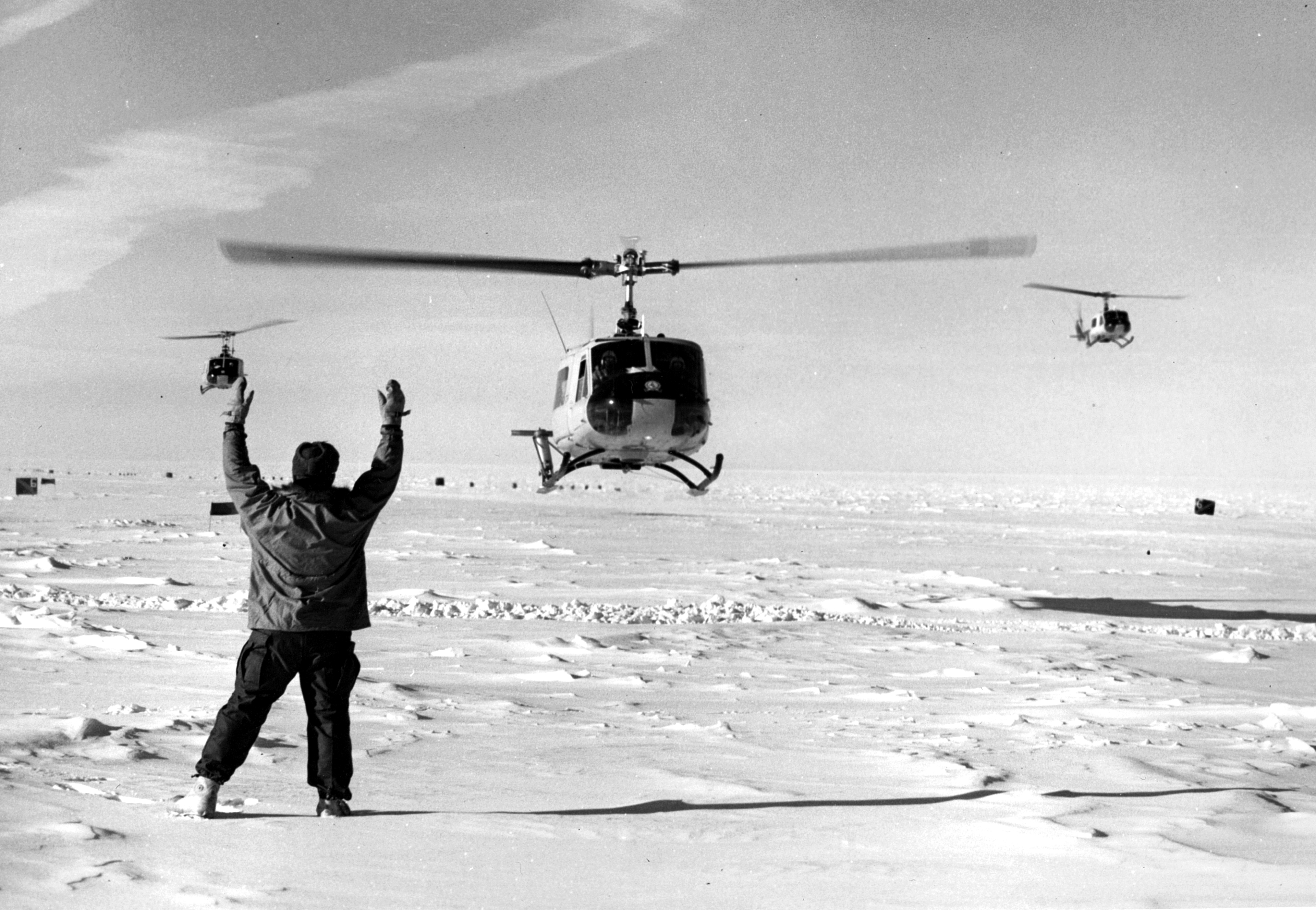 A man directs three helicopters where to land.