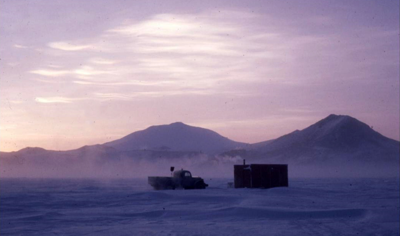 A truck and a building on an ice surface at sunrise.