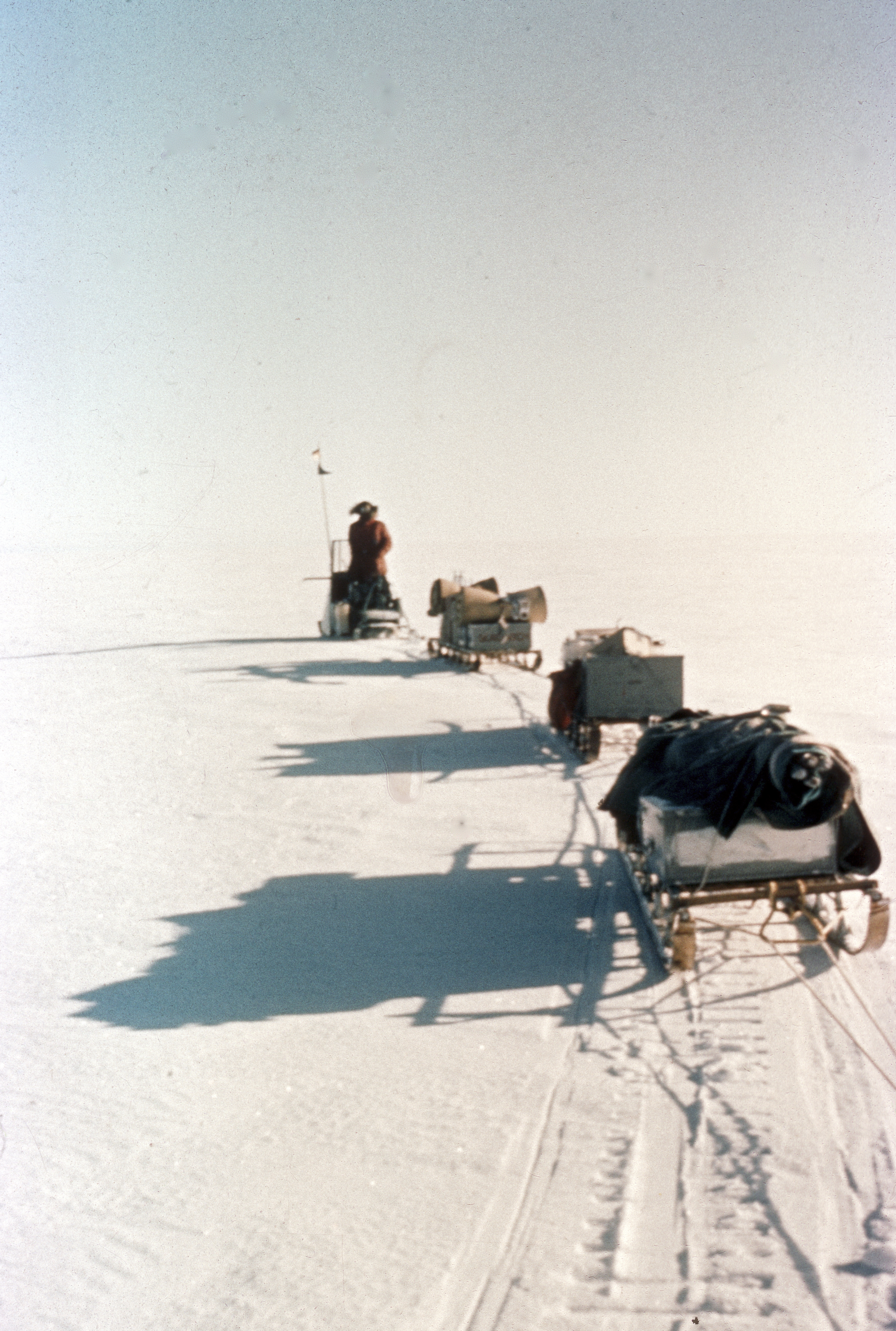 An old photo of a snowmobile pulling three sleds.