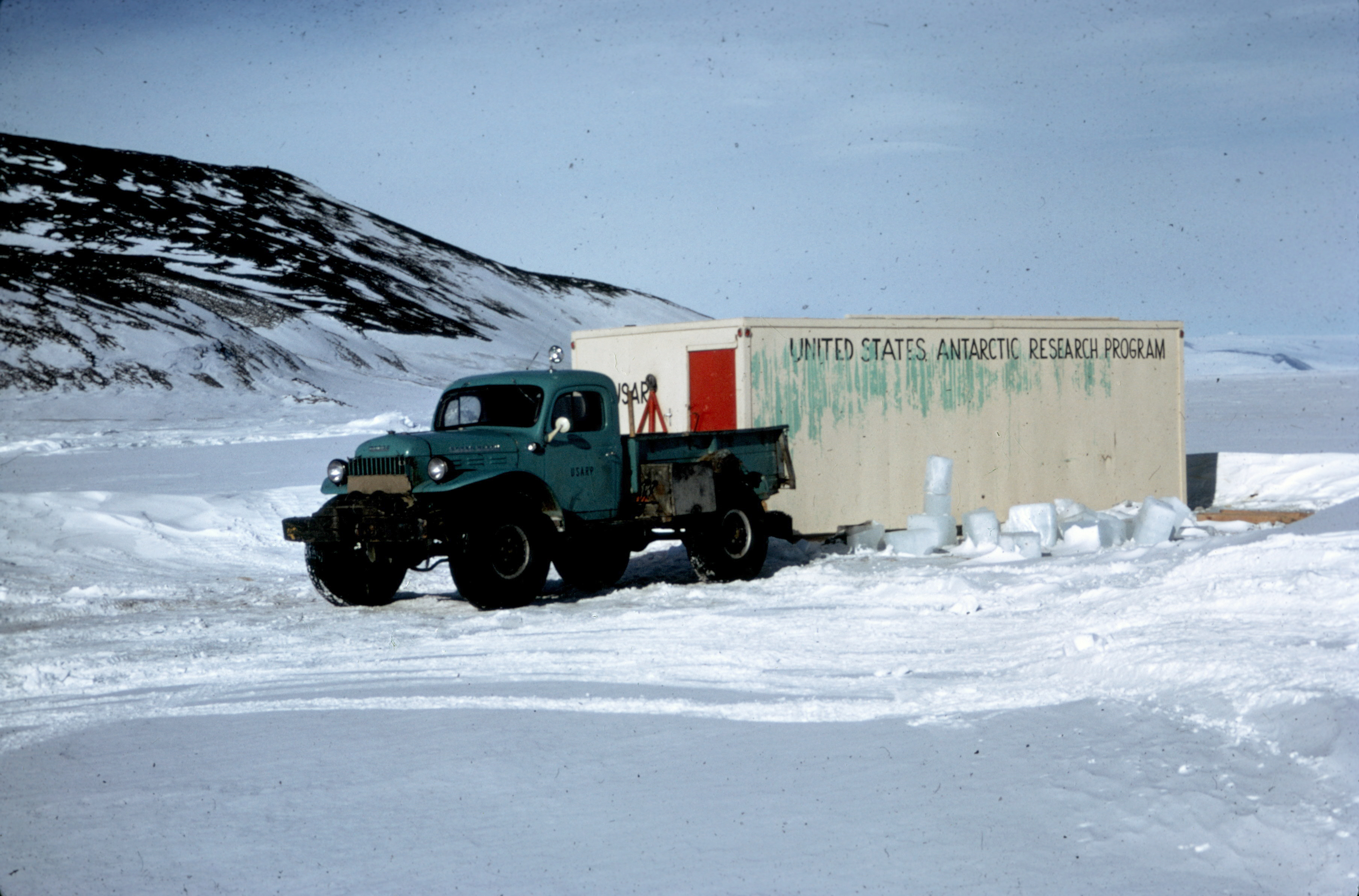 A pickup truck parked on ice near a hut.