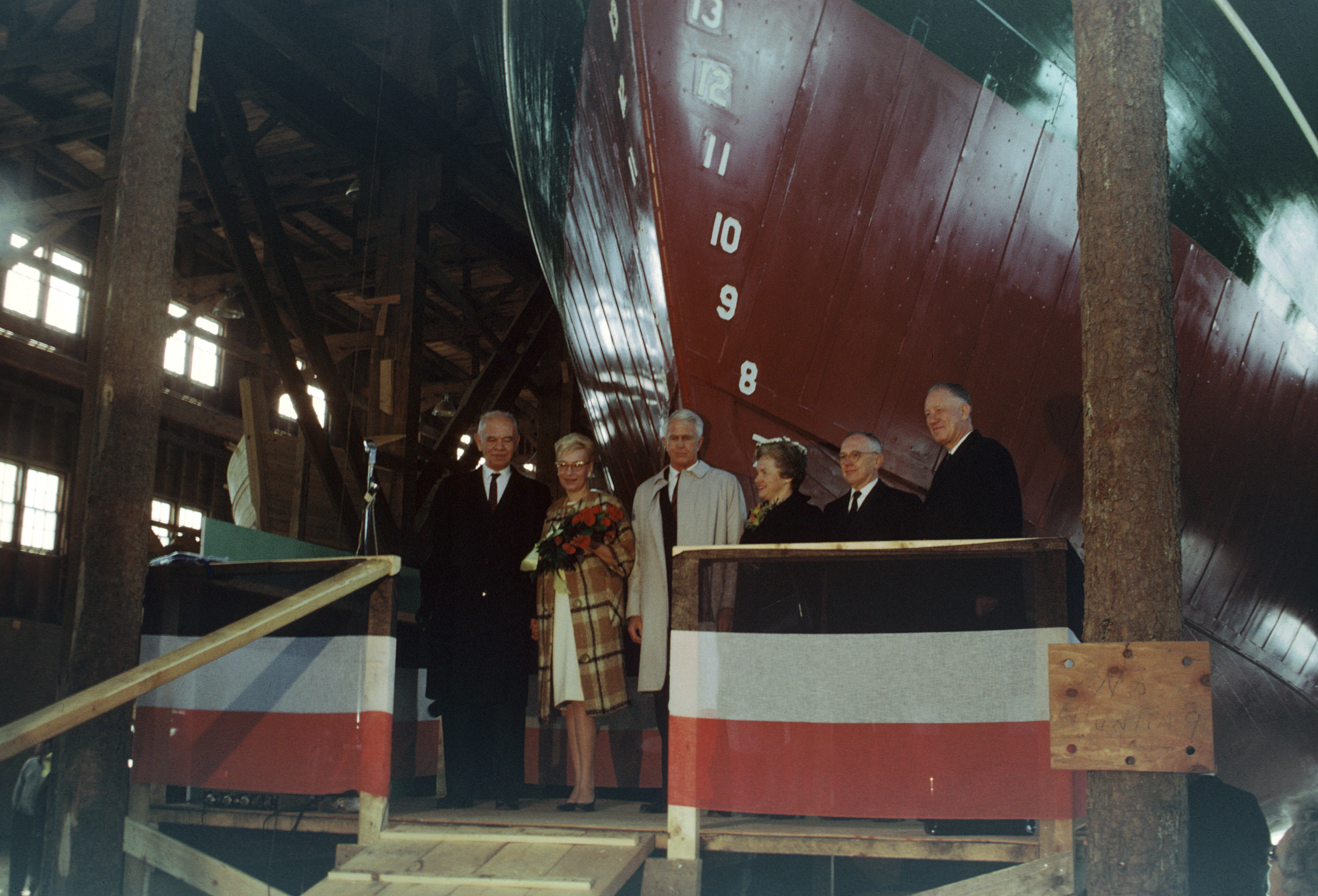 Six people dressed in formal attire about to christen a ship.