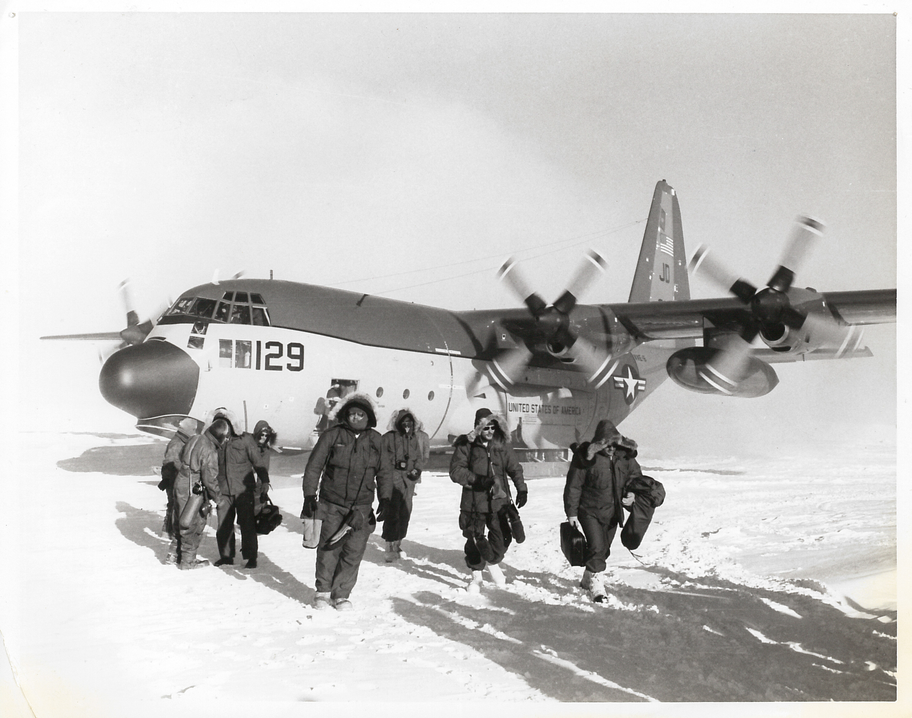 A group of men in parkas in front of an airplane that has landed on the snow.