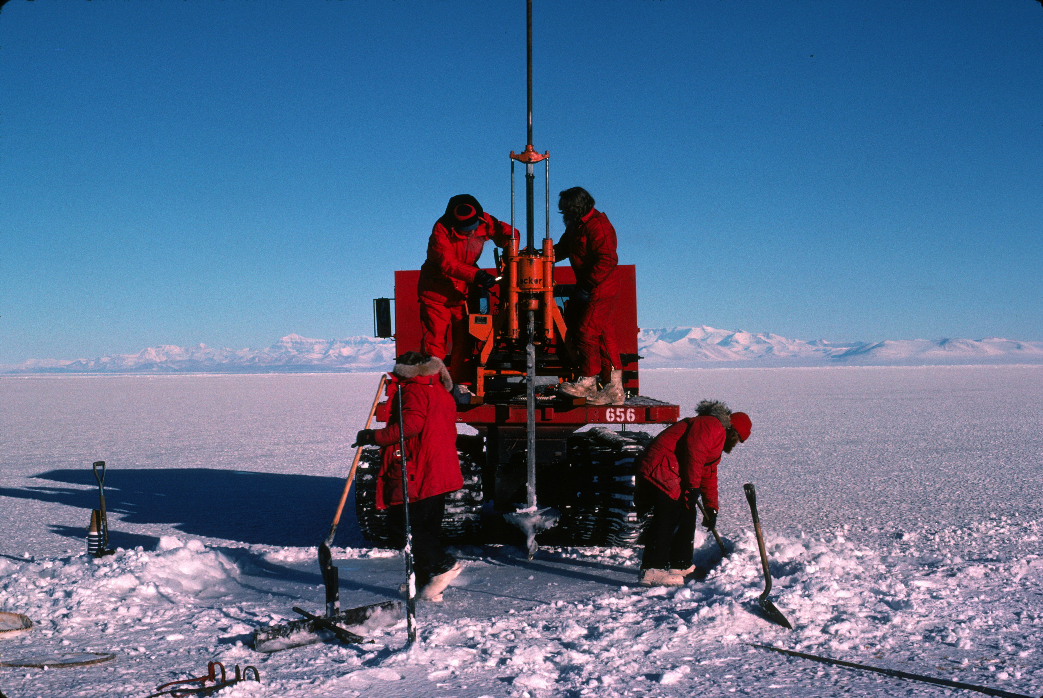 People working with a large drill on an icy surface.