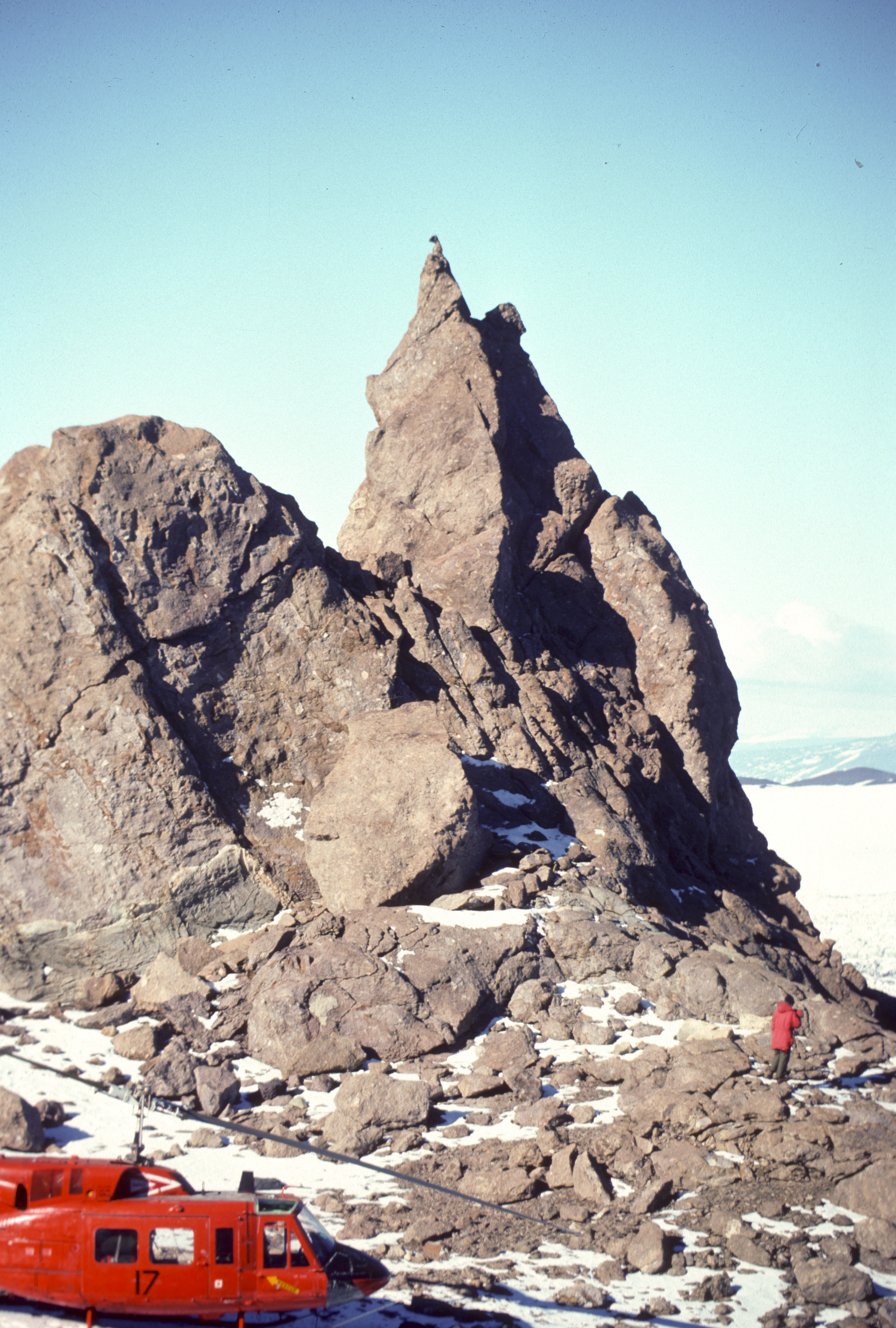 A helicopter by a tall rocky outcropping.