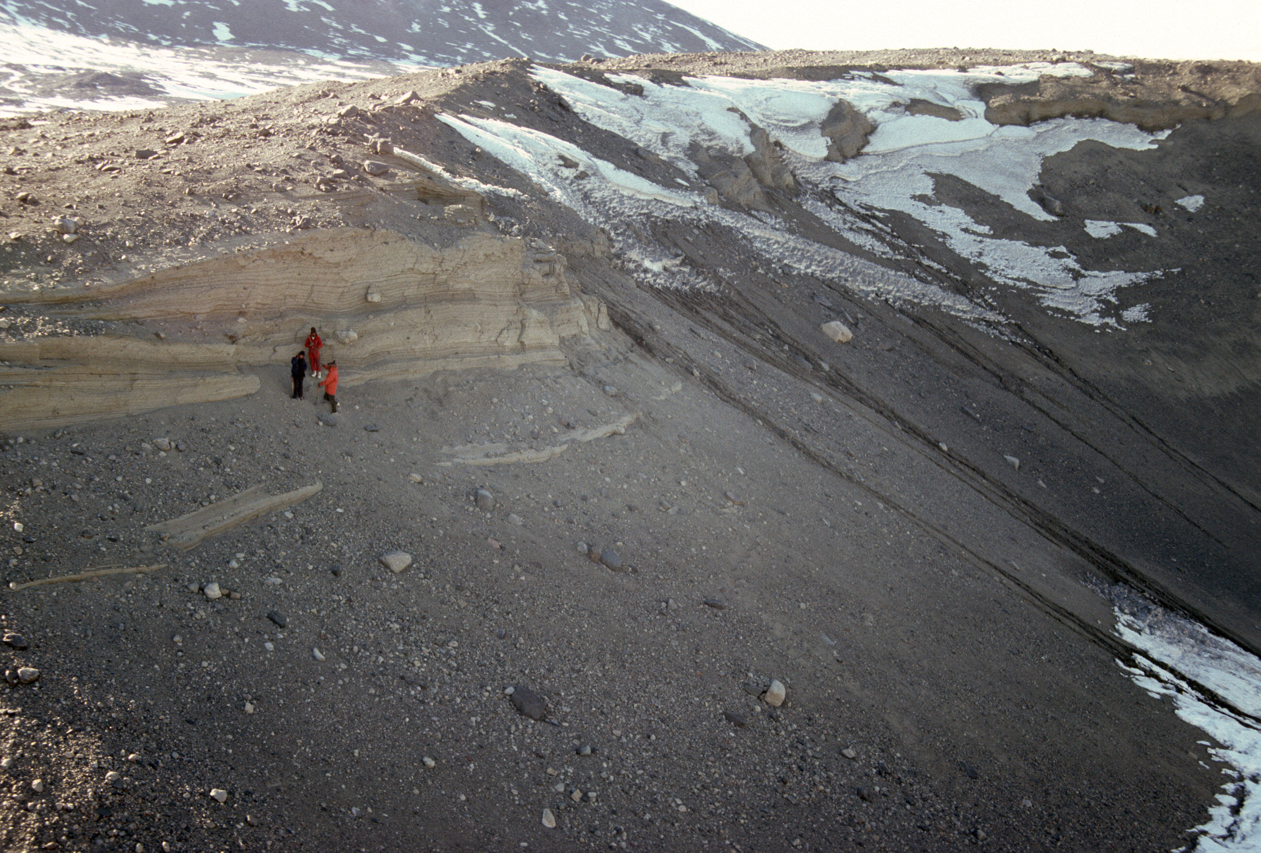 Three people standing at the top of a rocky mountainside.