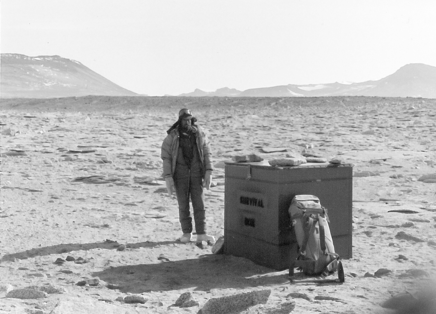 A man standing next to a box on a wide open space.
