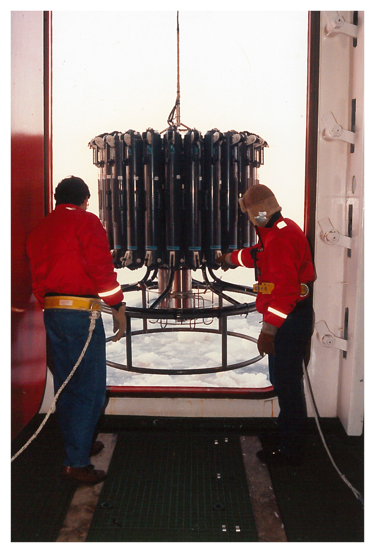 Two people lowering an instrument over the side of a ship.